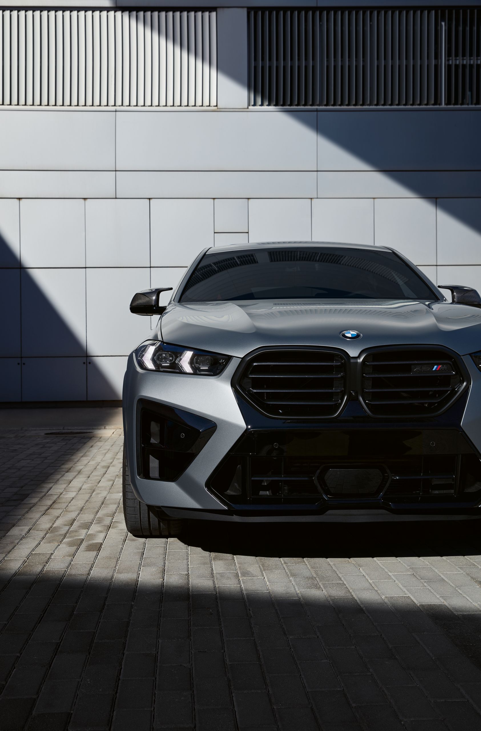 Front view of a BMW X6 M Competition parked in front of a grey wall