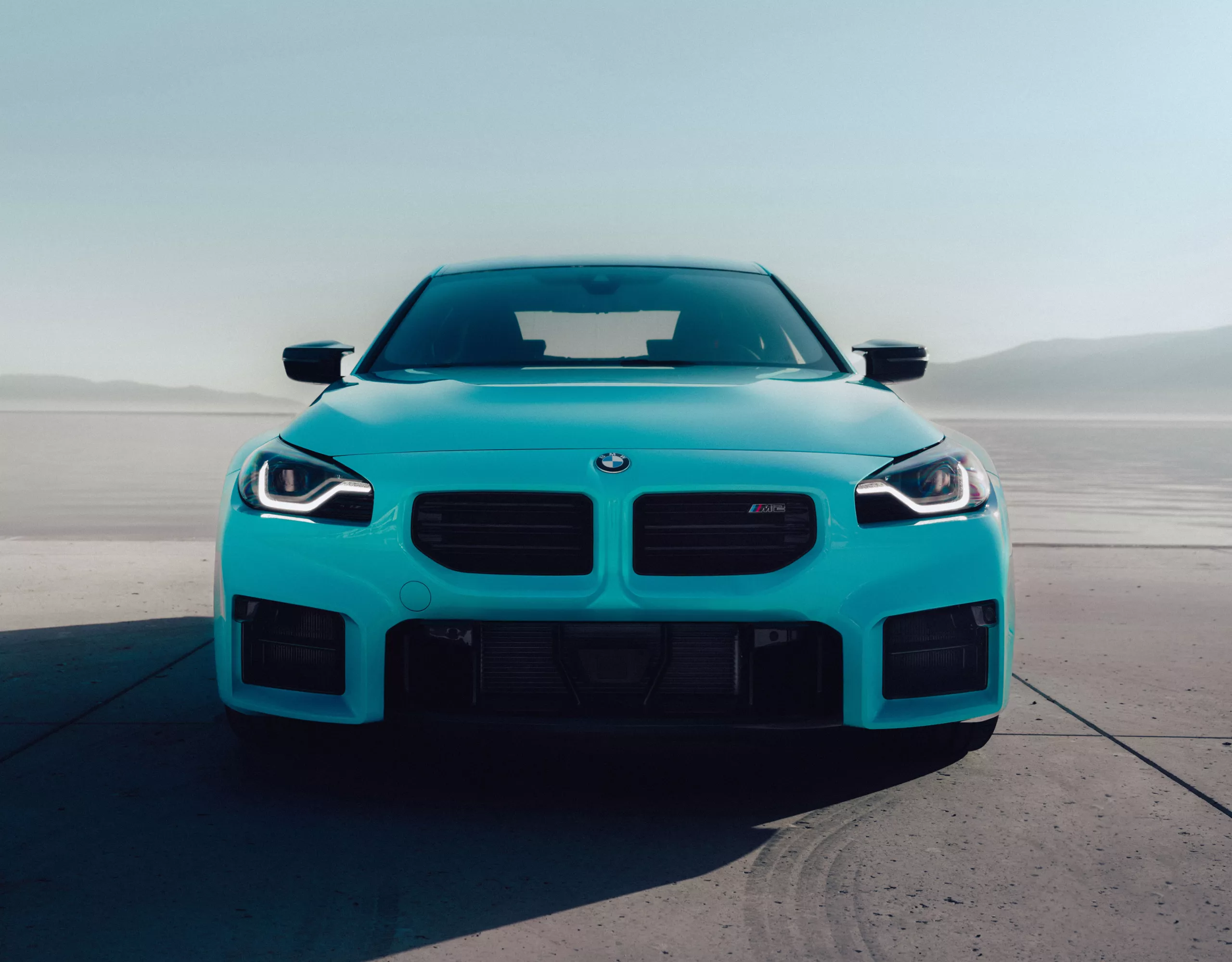 A bold image of the M2 with M xDrive head-on, with a shadow cast on a desert floor.