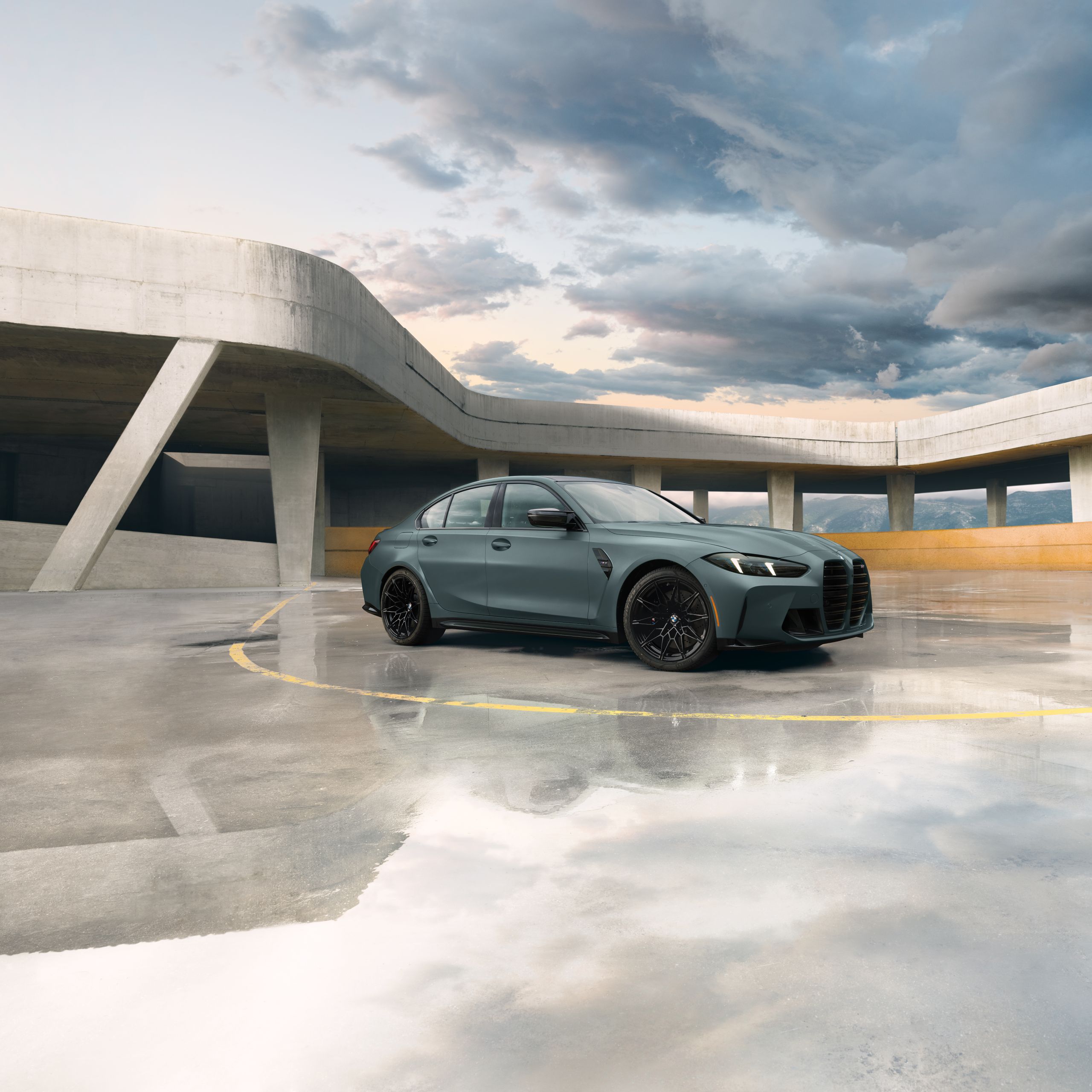 Angled view of the BMW M3 Sedan in a parking garage with mountains in the distance