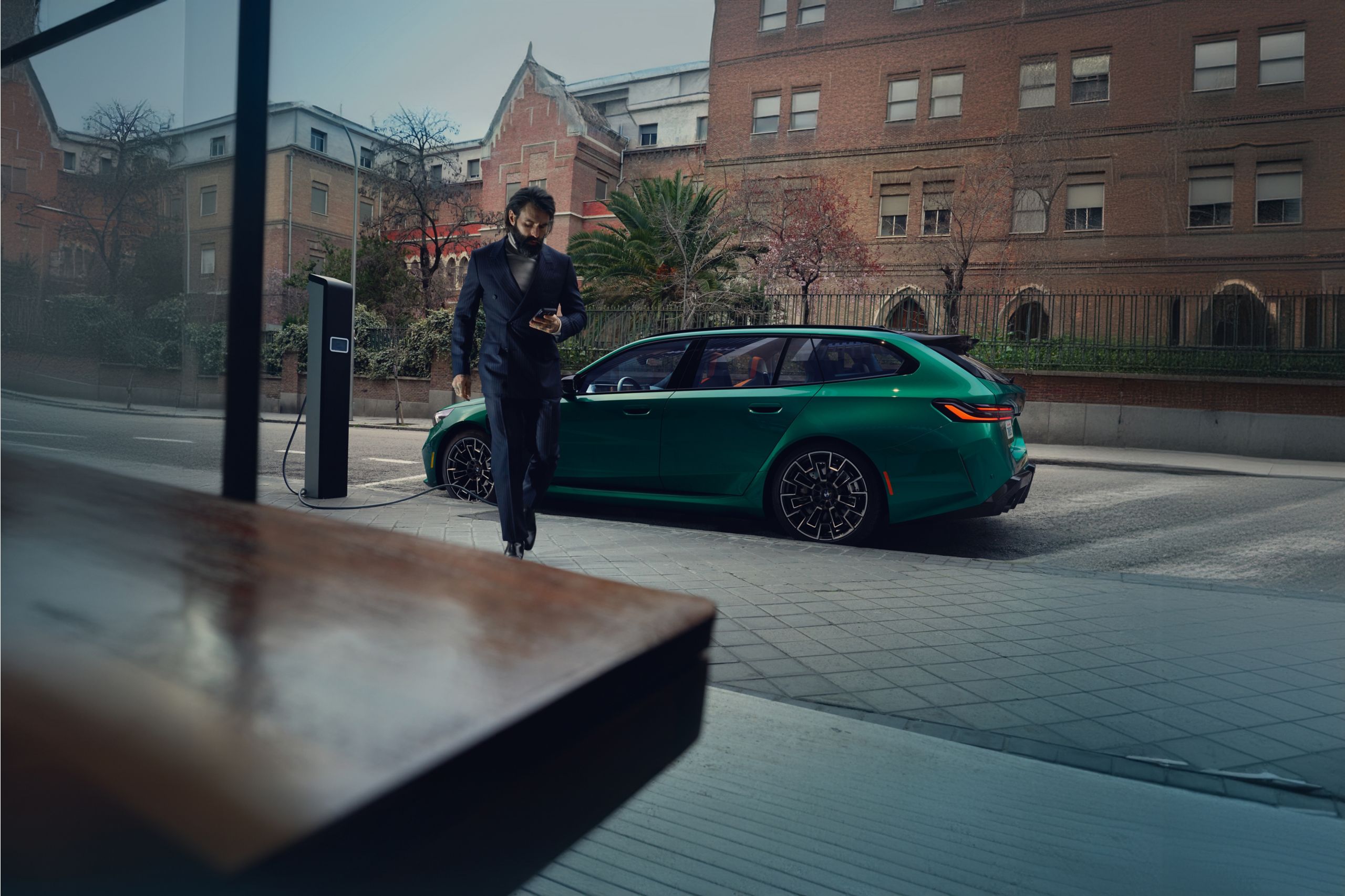 A man walks away from his BMW M5 Touring as it charges at a public charging station.