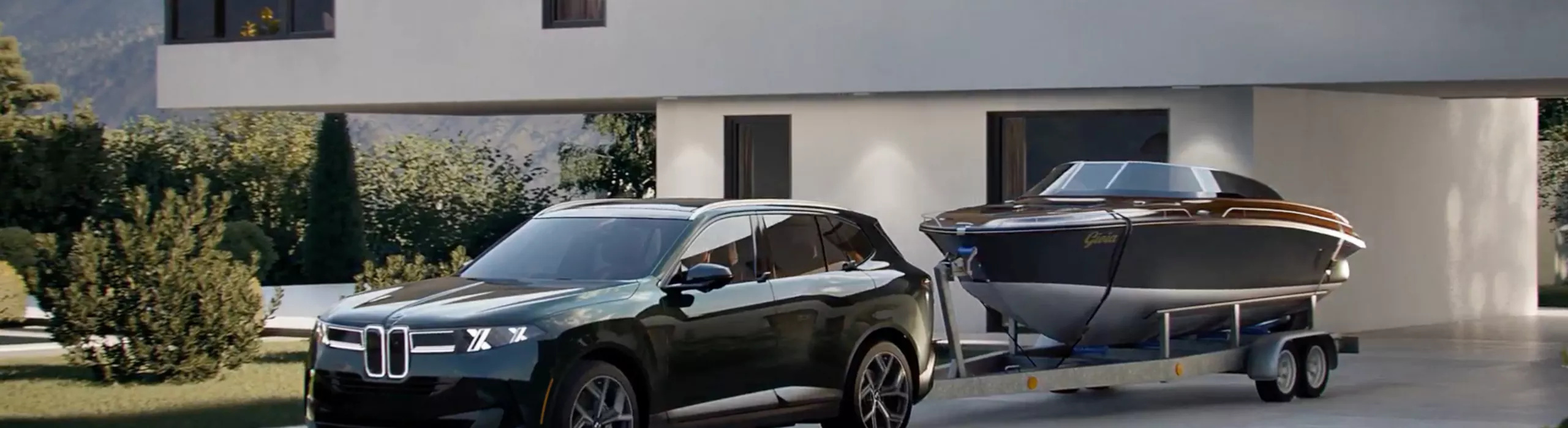 The BMW X5 sits in a driveway of a modern home with a boat on a trailer attached ot the tow hitch.