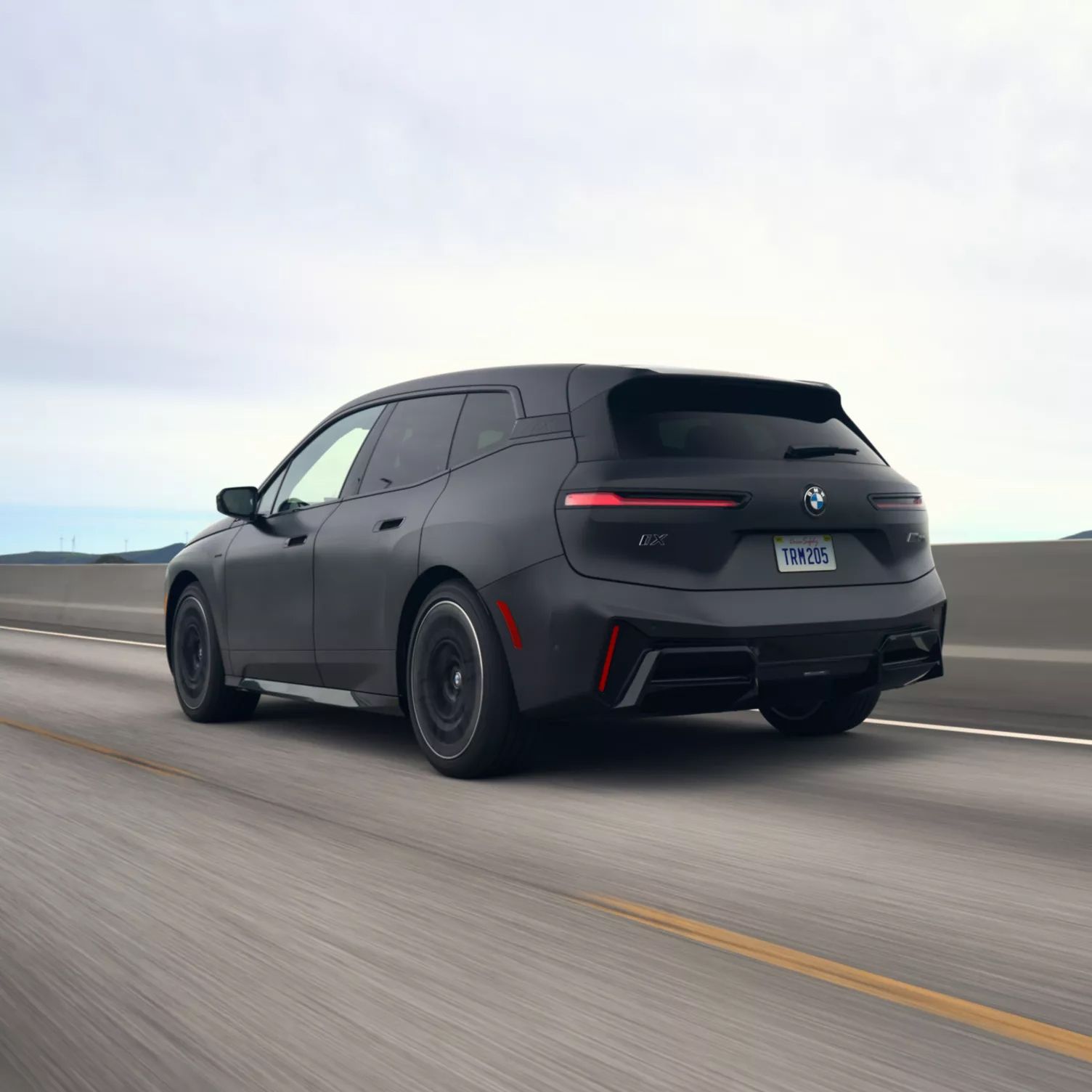 A rear shot quarter shot of the BMW iX driving down the highway.