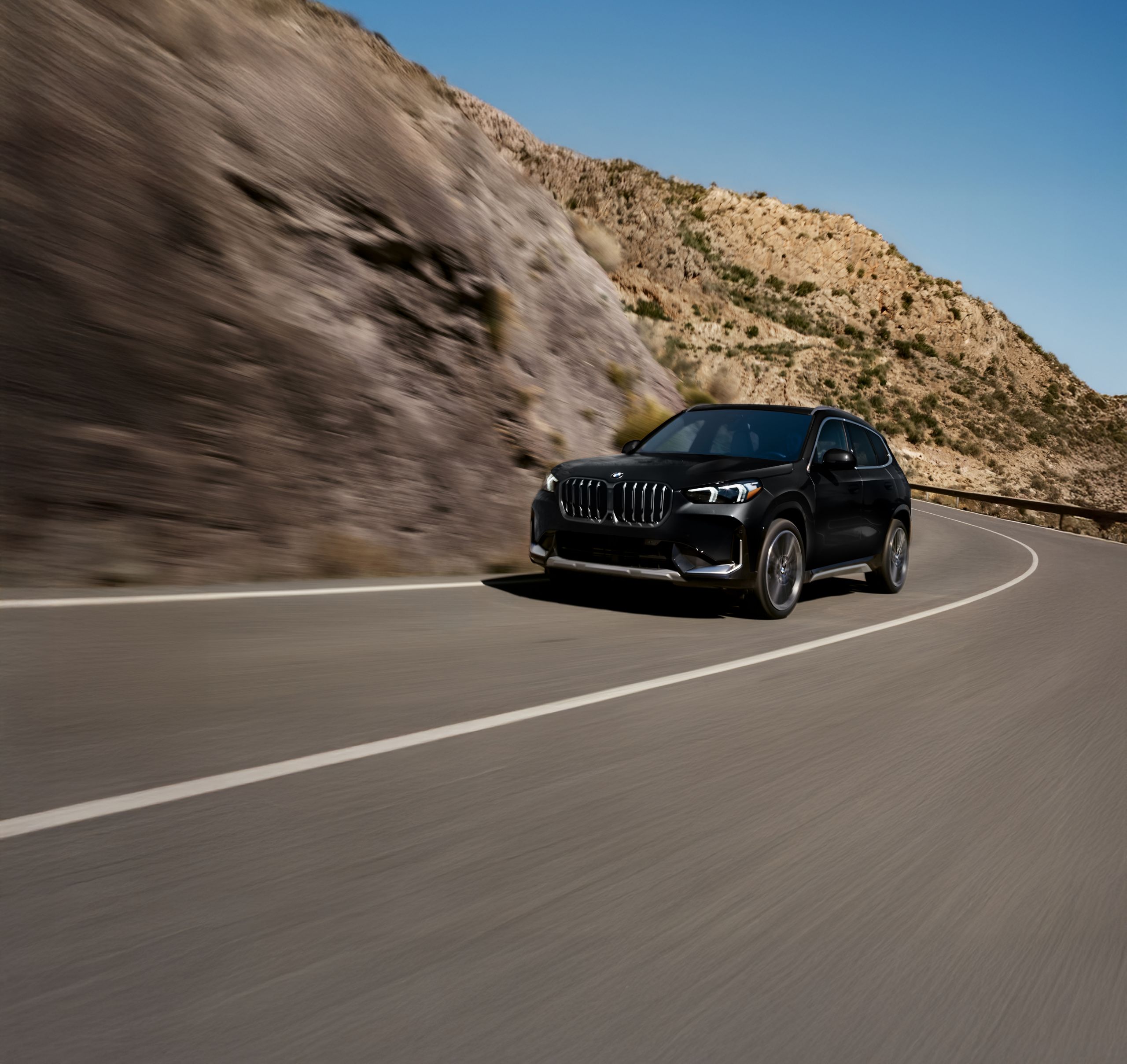 The BMW X1 xDrive28i driving along a winding mountain road under a clear blue sky.