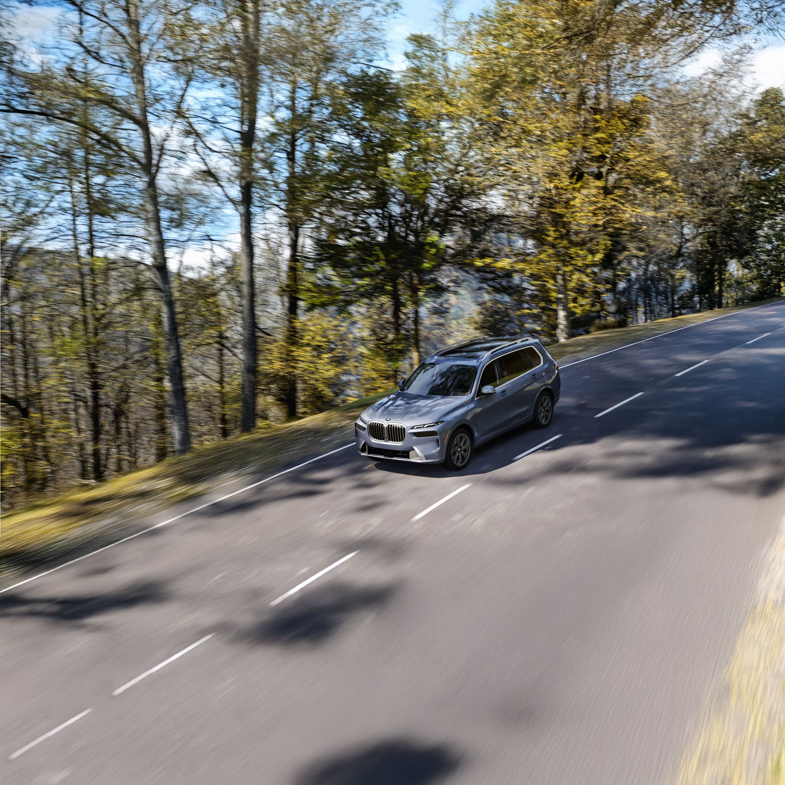 The BMW X7 xDrive40i driving down a curving hill with scenic woodlands in the background.