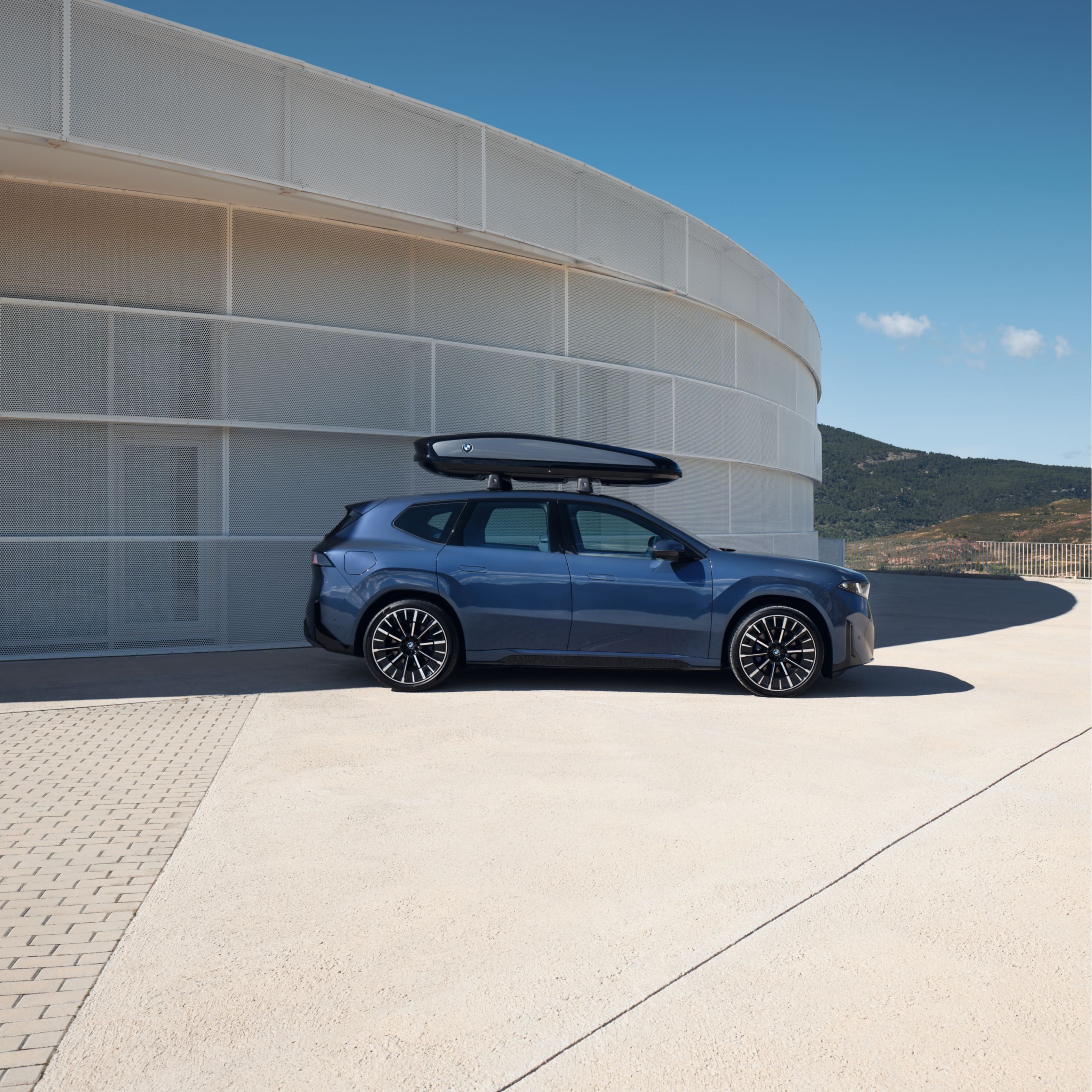 A BMW iX3 with a roof rack mount is parked on a parking deck in front of a mountain vista