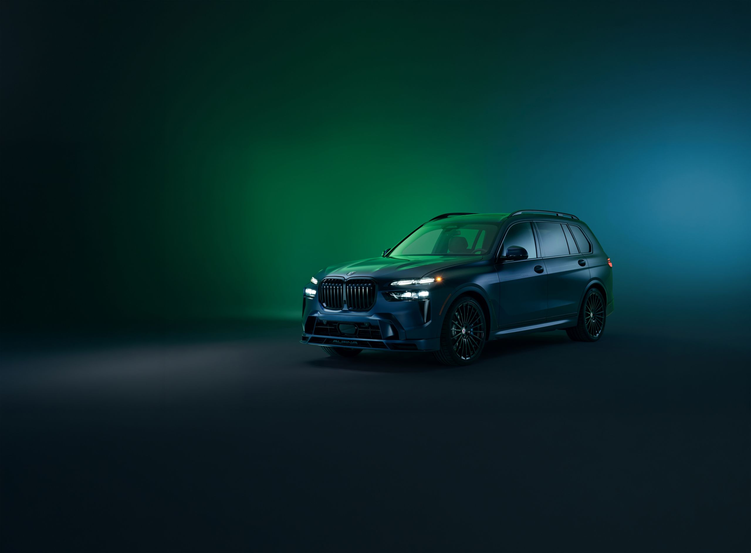 The BMW ALPINA XB7 MANUFAKTUR parked in a studio space with a green and blue gradient background 