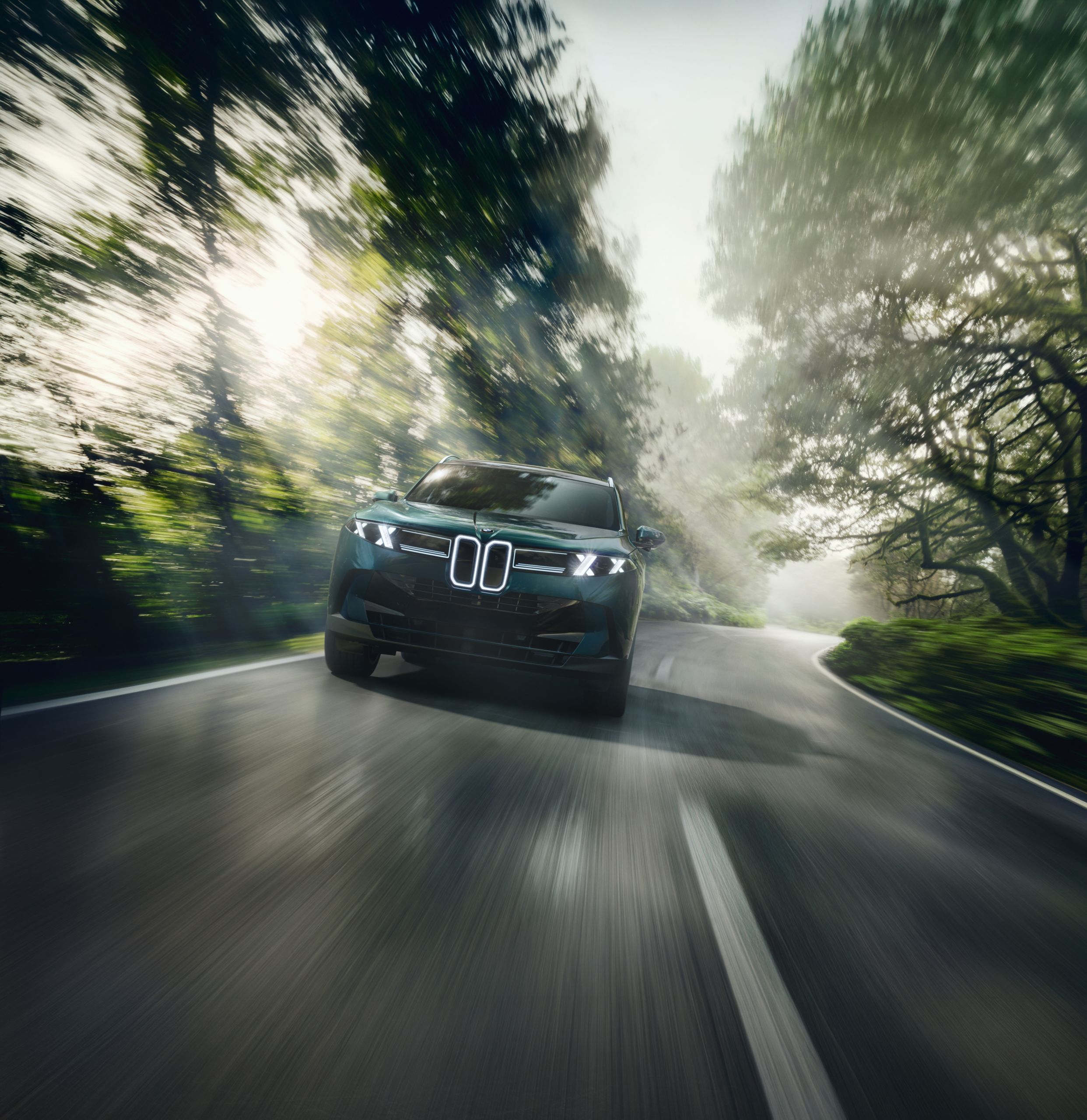 A BMW X5 drives on a highway through a wooded area.