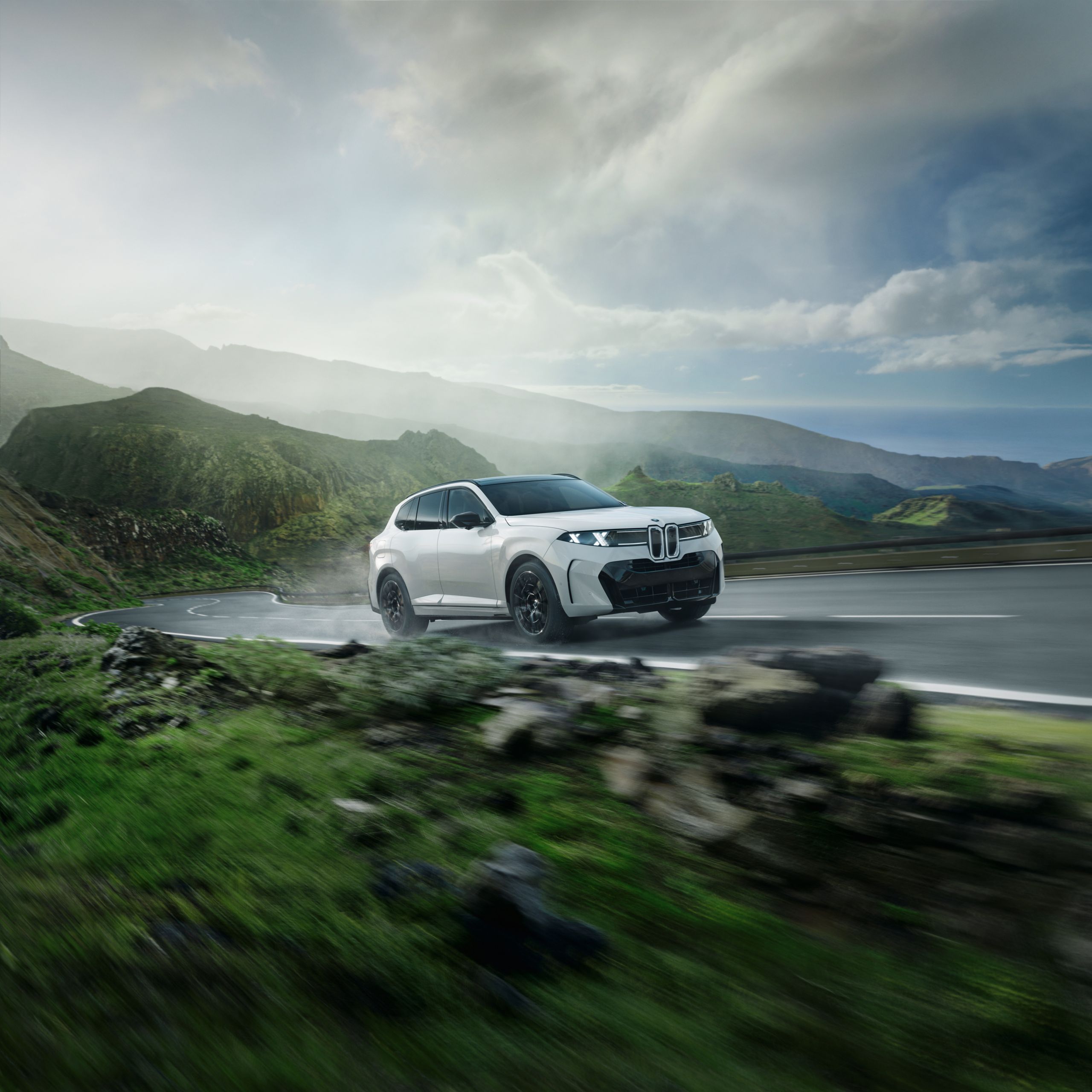 A BMW X5 drives on a highway through a rocky coastal environment.