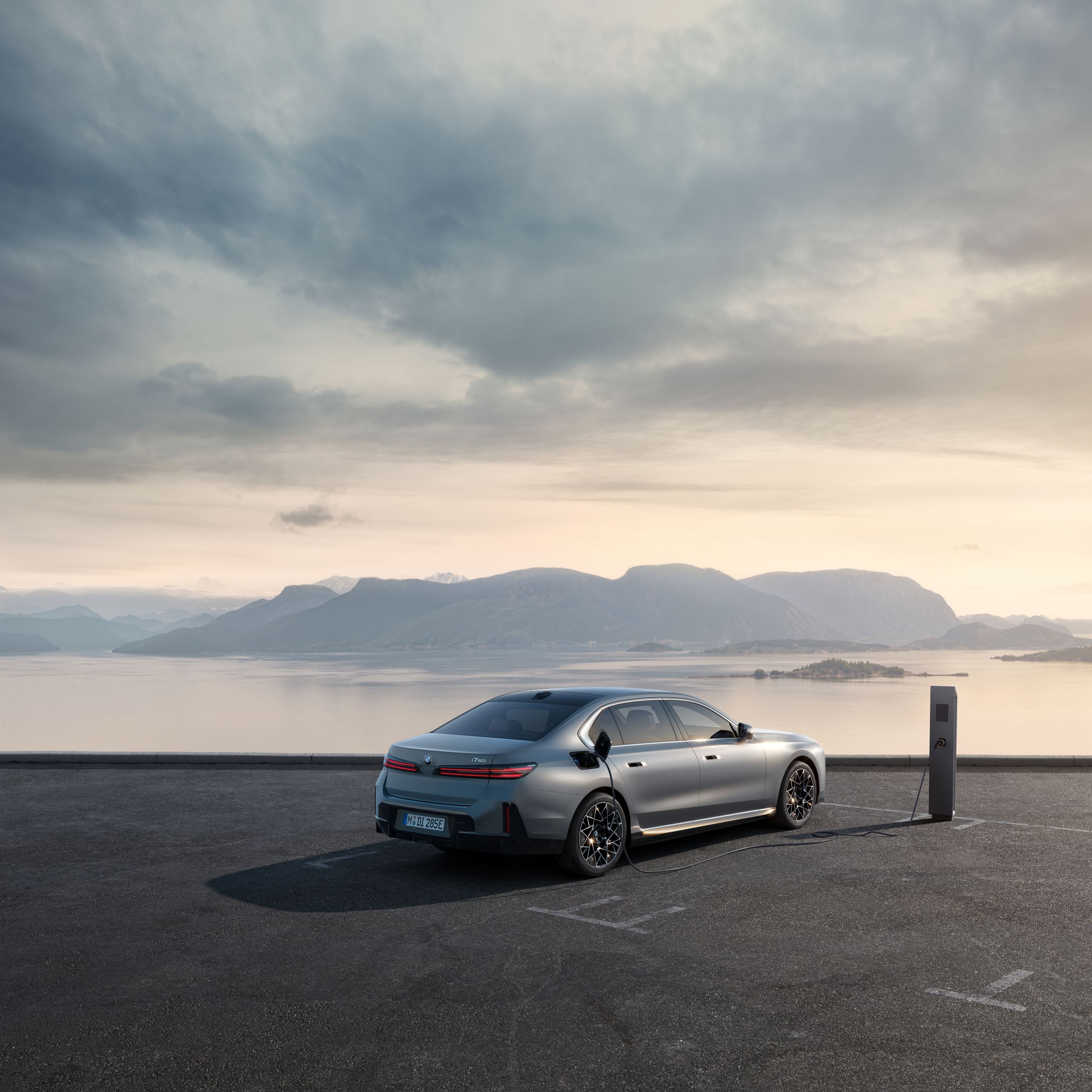 Vehicle is parked in front of a coastal landscape and is charging at a charging post.