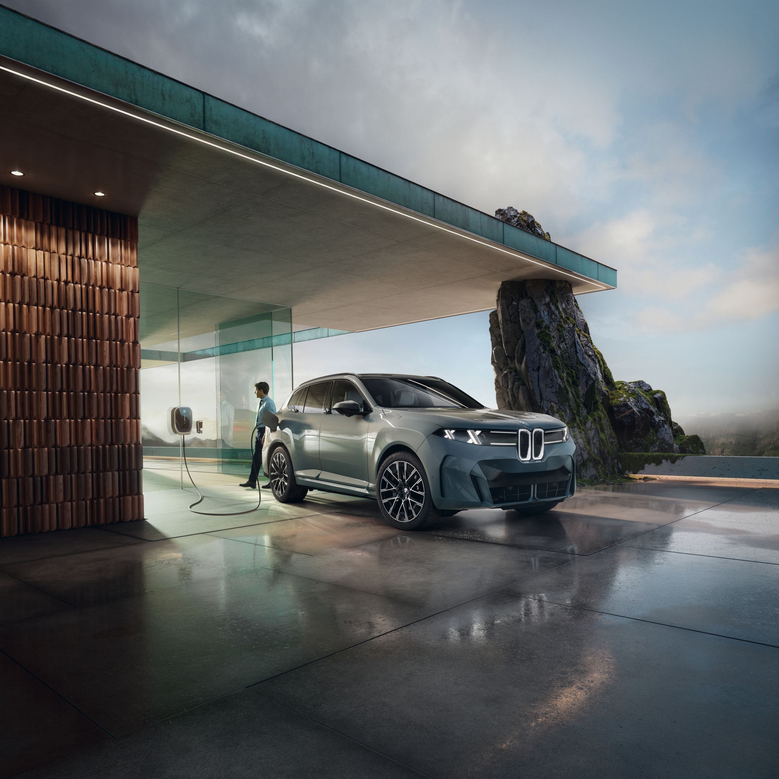 A man stands by while his BMW iX5 charges beneath a modern cement overhnag