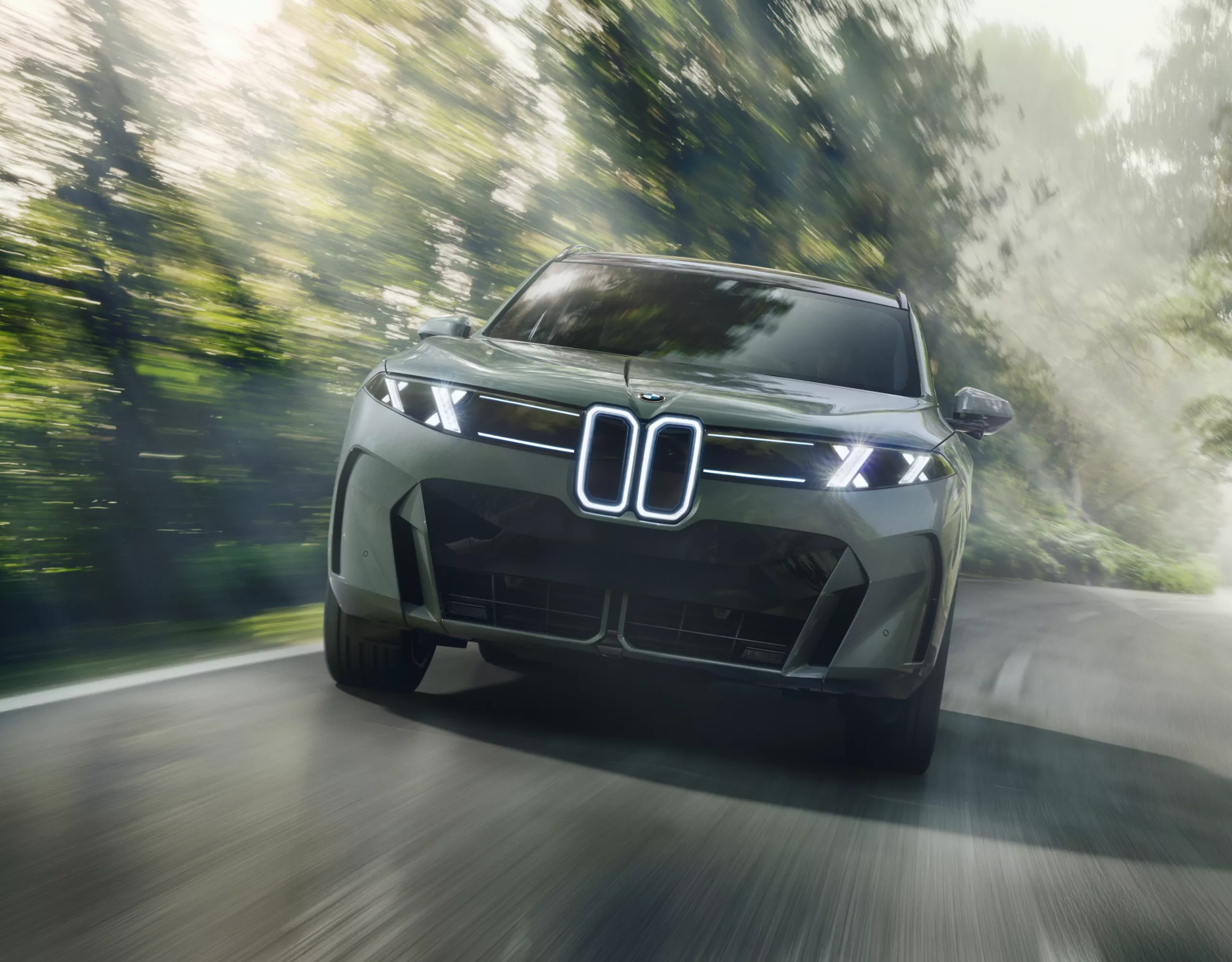 A BMW on a road between trees is driving towards the viewer