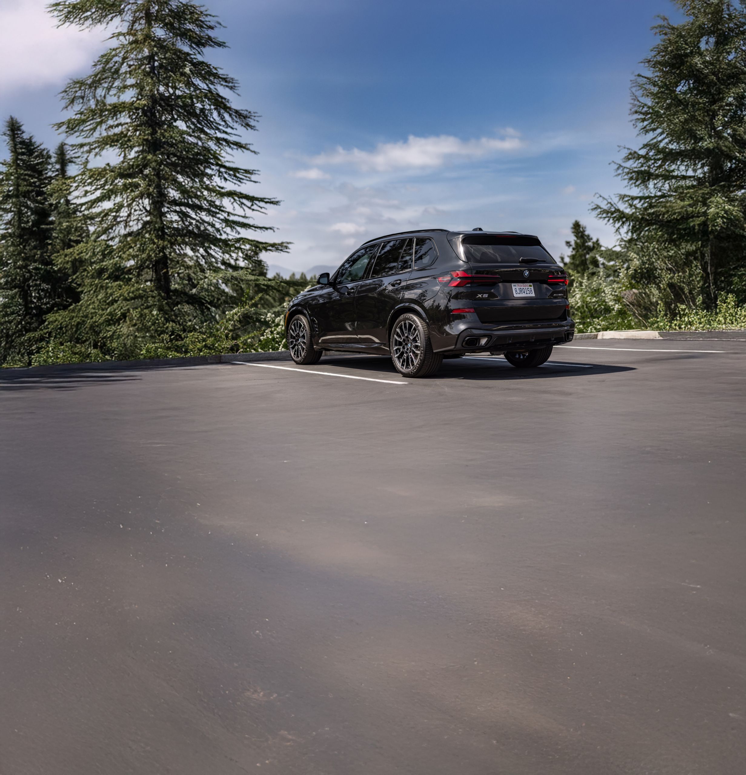 The BMW X5 xDrive50e parked in a parking lot by a forested area in summer.