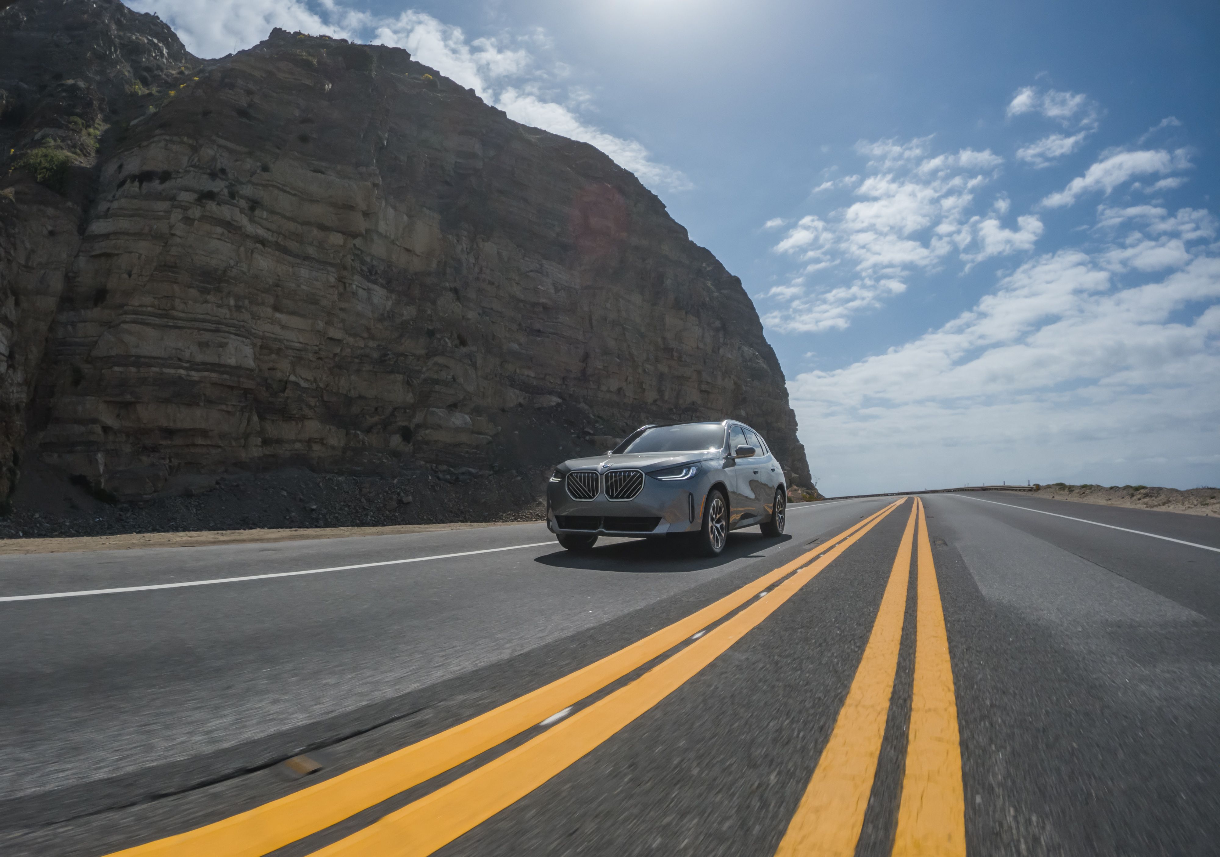 A dramatic shot of the BMW X3 30 xDrive driving down a scenic highway on a sunny day.