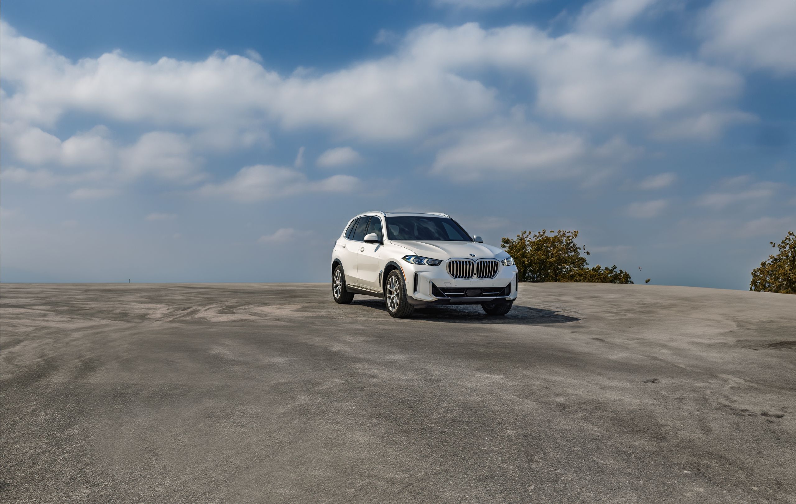 A BMW X5 parked on a broad expanse of concrete with a blue sky in the background
