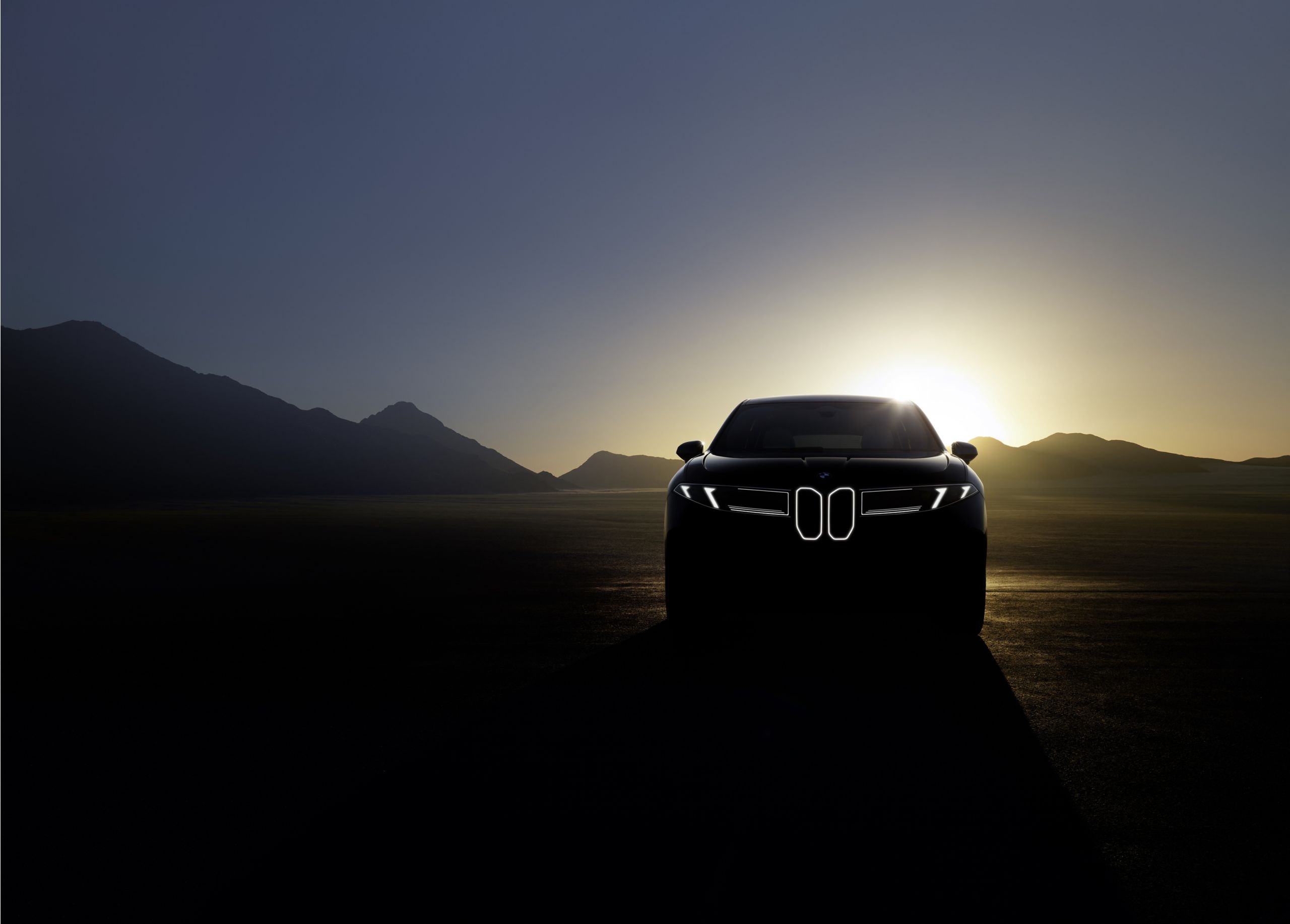 Una BMW iX è parcheggiata in un parcheggio davanti a un edificio per uffici ed è collegata a una stazione di ricarica