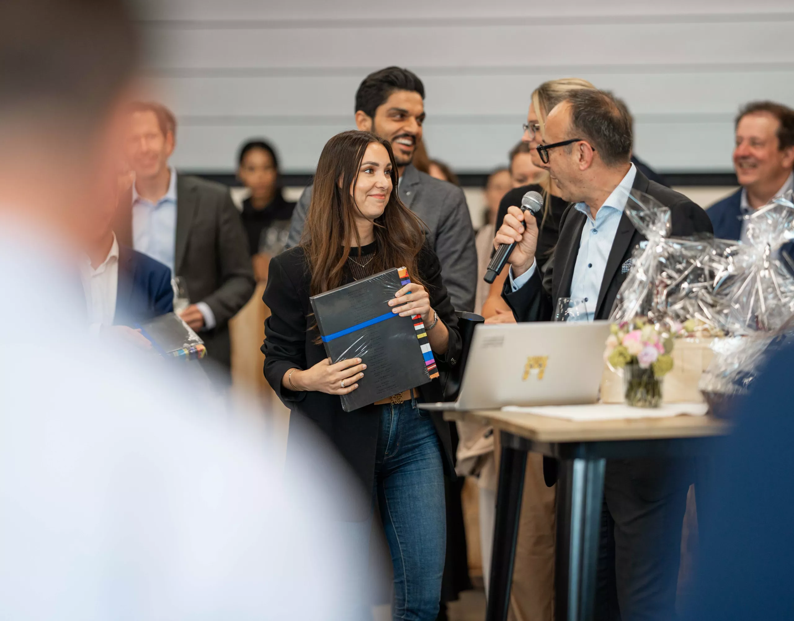 Un moderatore con un microfono e una donna con un libro in mano si guardano fianco a fianco in occasione di un evento per i collaboratori