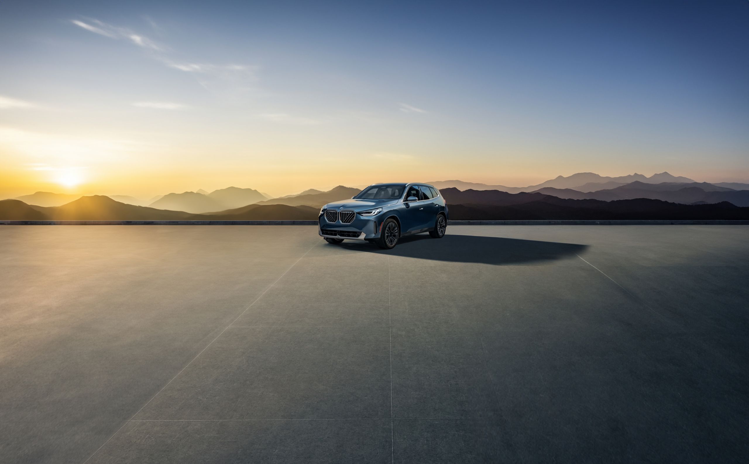 A BMW X3 parked on a concrete platform overlooking a shaded forest landscape at dusk