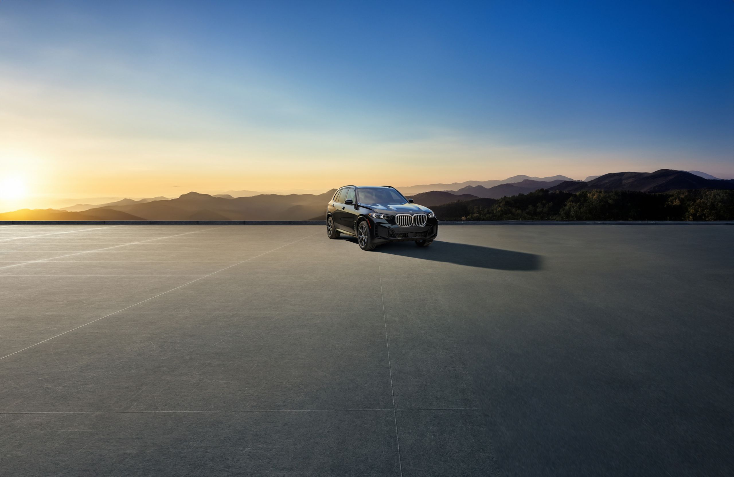 A BMW X5 parked on a concrete platform overlooking a shaded forest landscape at dusk