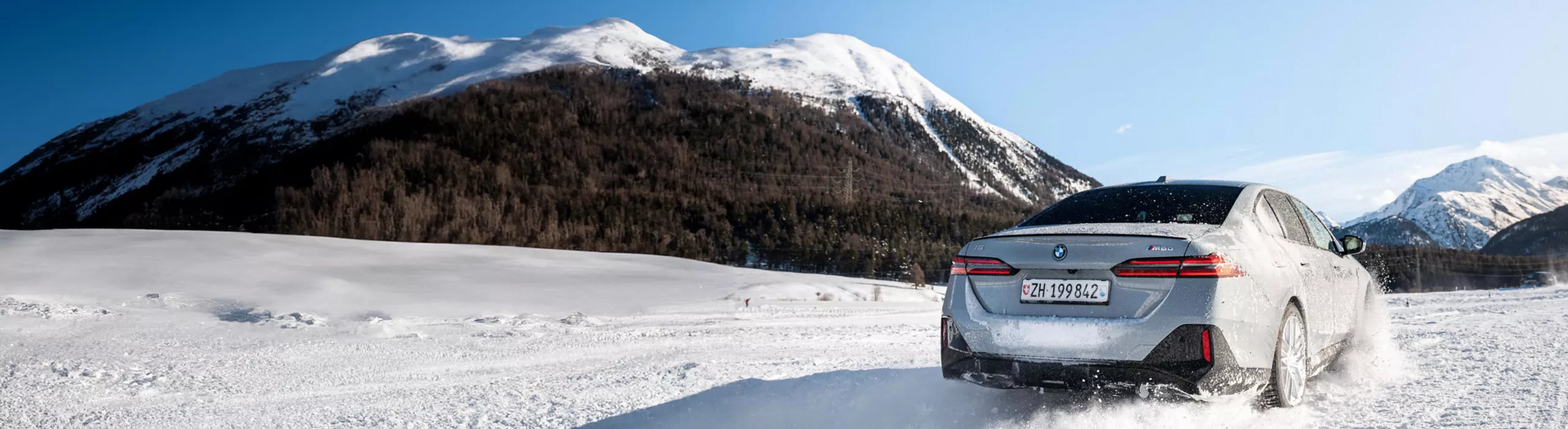 BMW i5 fährt dynamisch durch eine verschneite Winterlandschaft