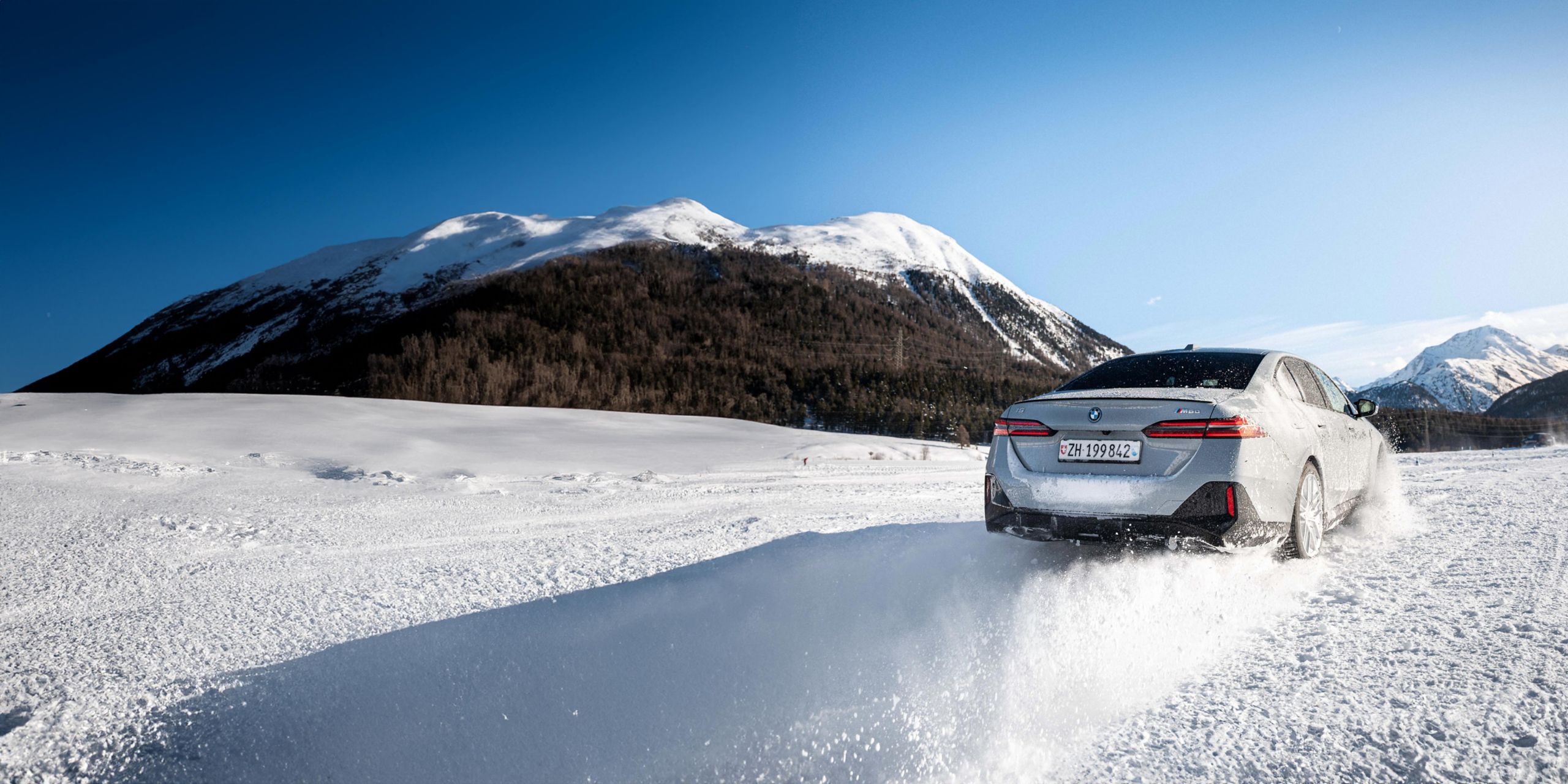BMW i5 fährt dynamisch durch eine verschneite Winterlandschaft