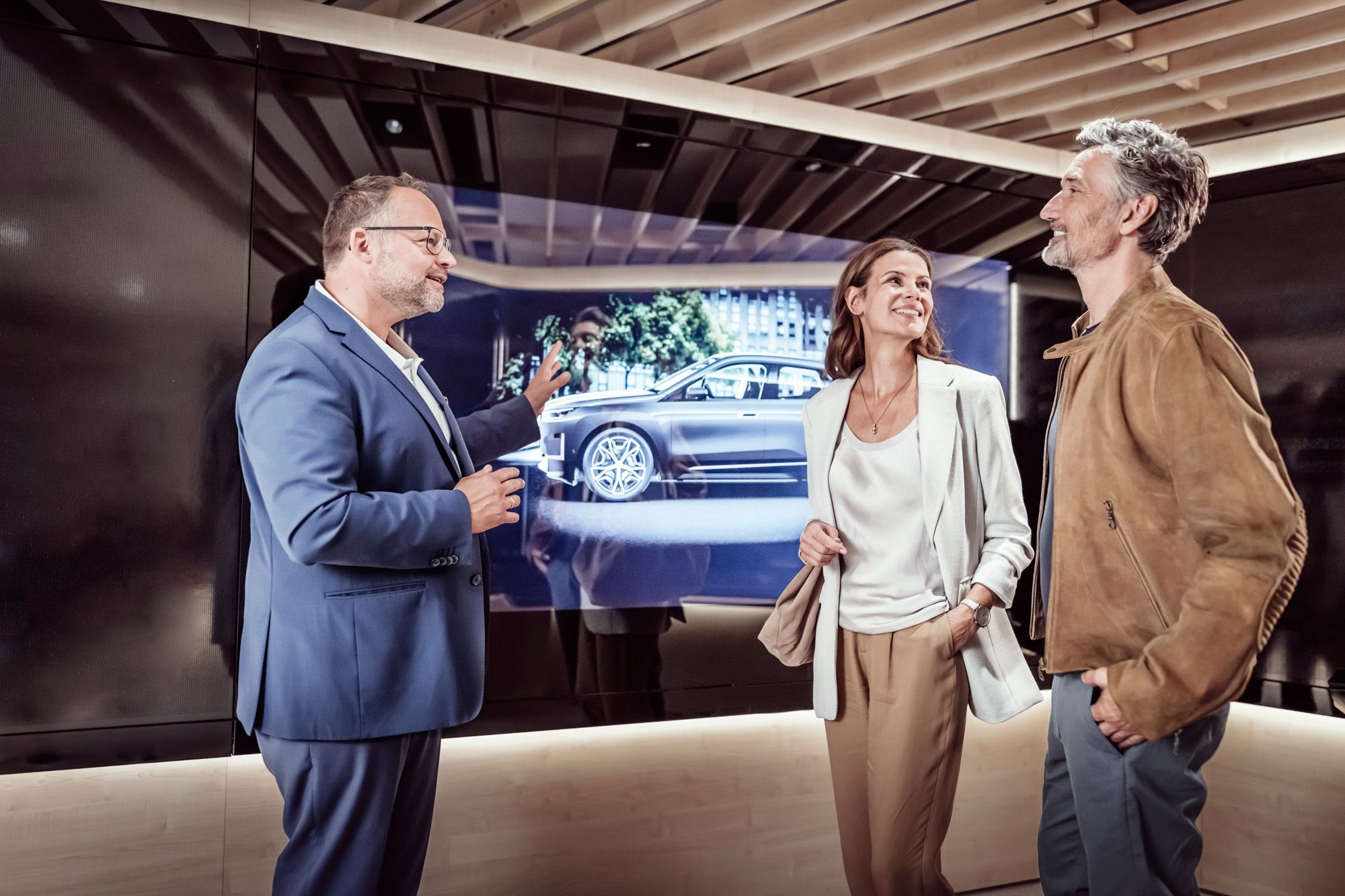 Fahrzeugexperte zeigt glücklichem Paar die virtuelle Animation Ihres BMW im Product Info Center