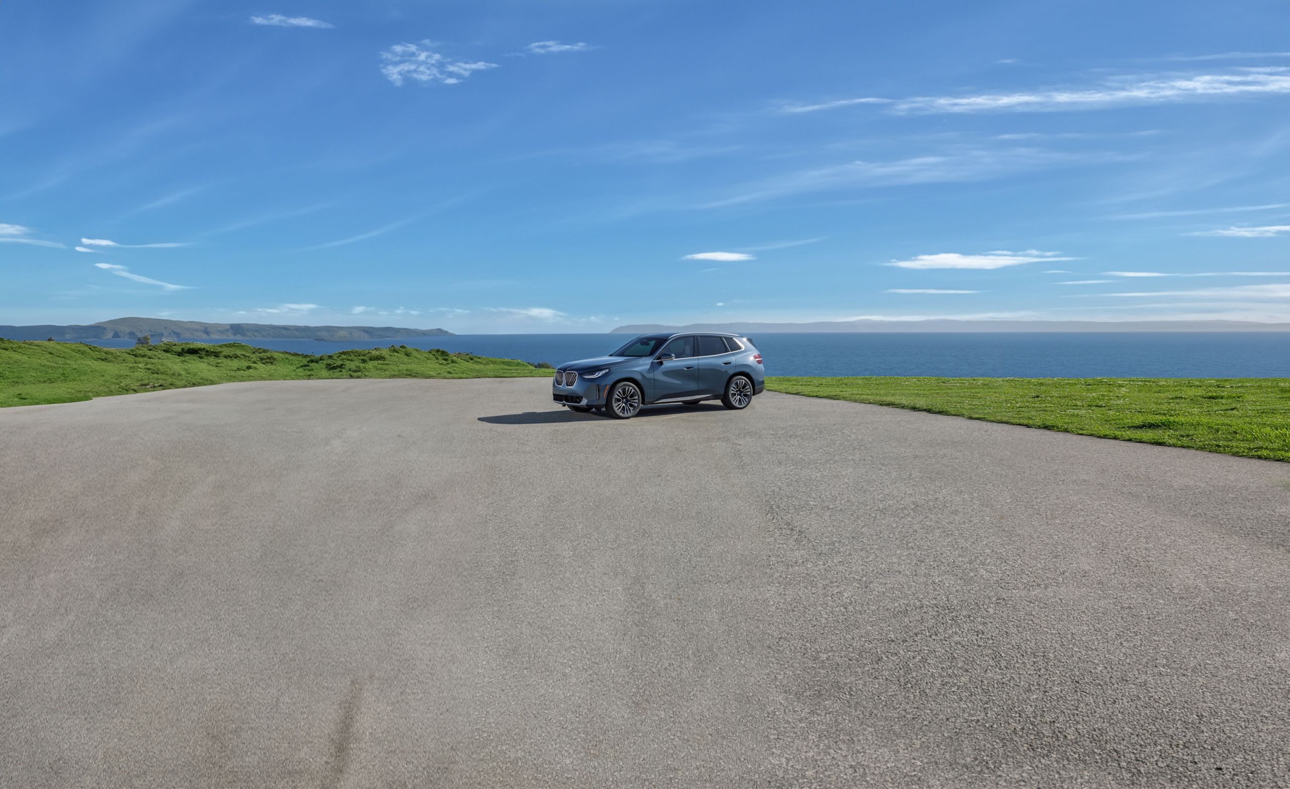 A BMW X3 parked on a broad expanse of concrete with a blue sky and green fields in the background