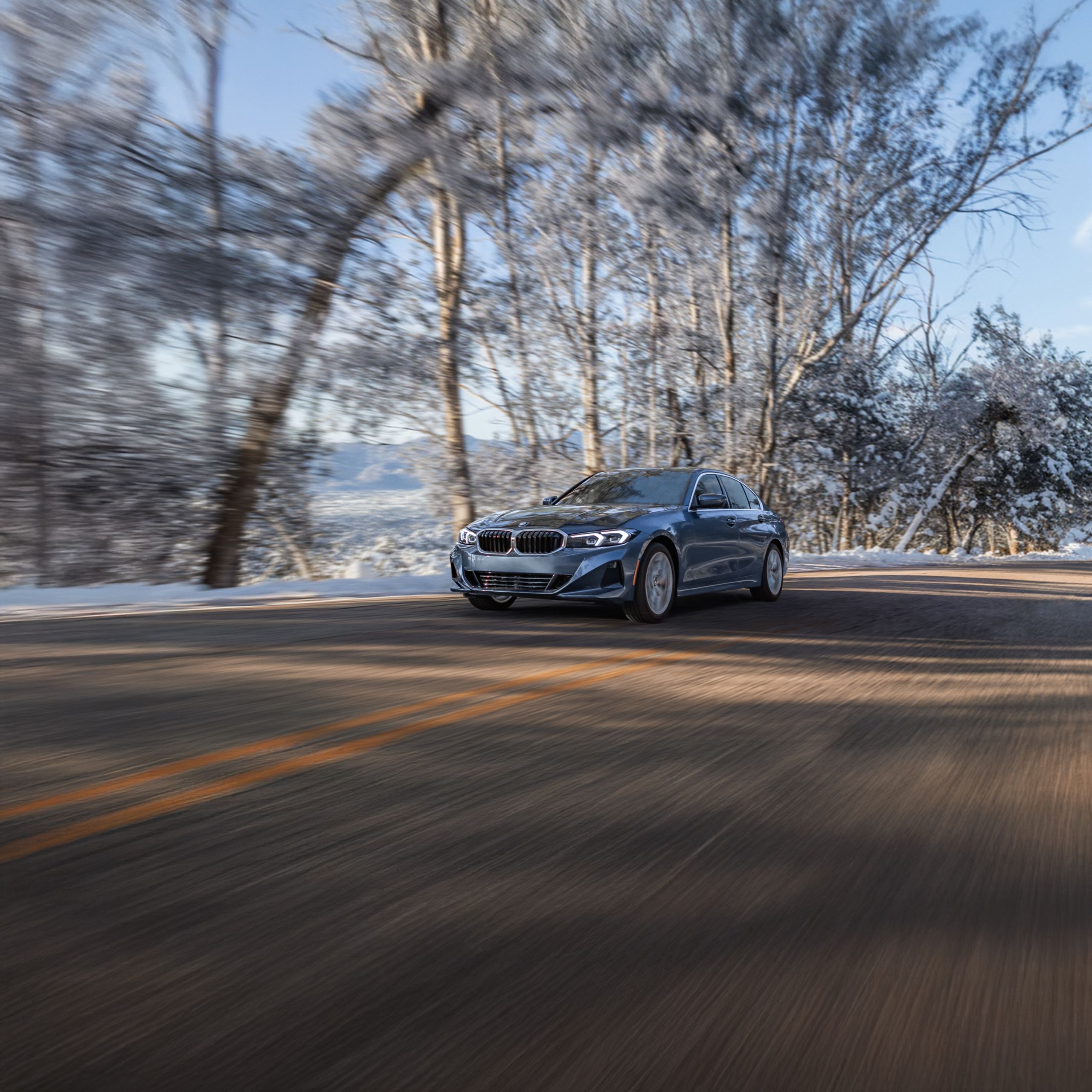 Heroic shot of the BMW 330i xDrive driving on a snowy tree-lined road