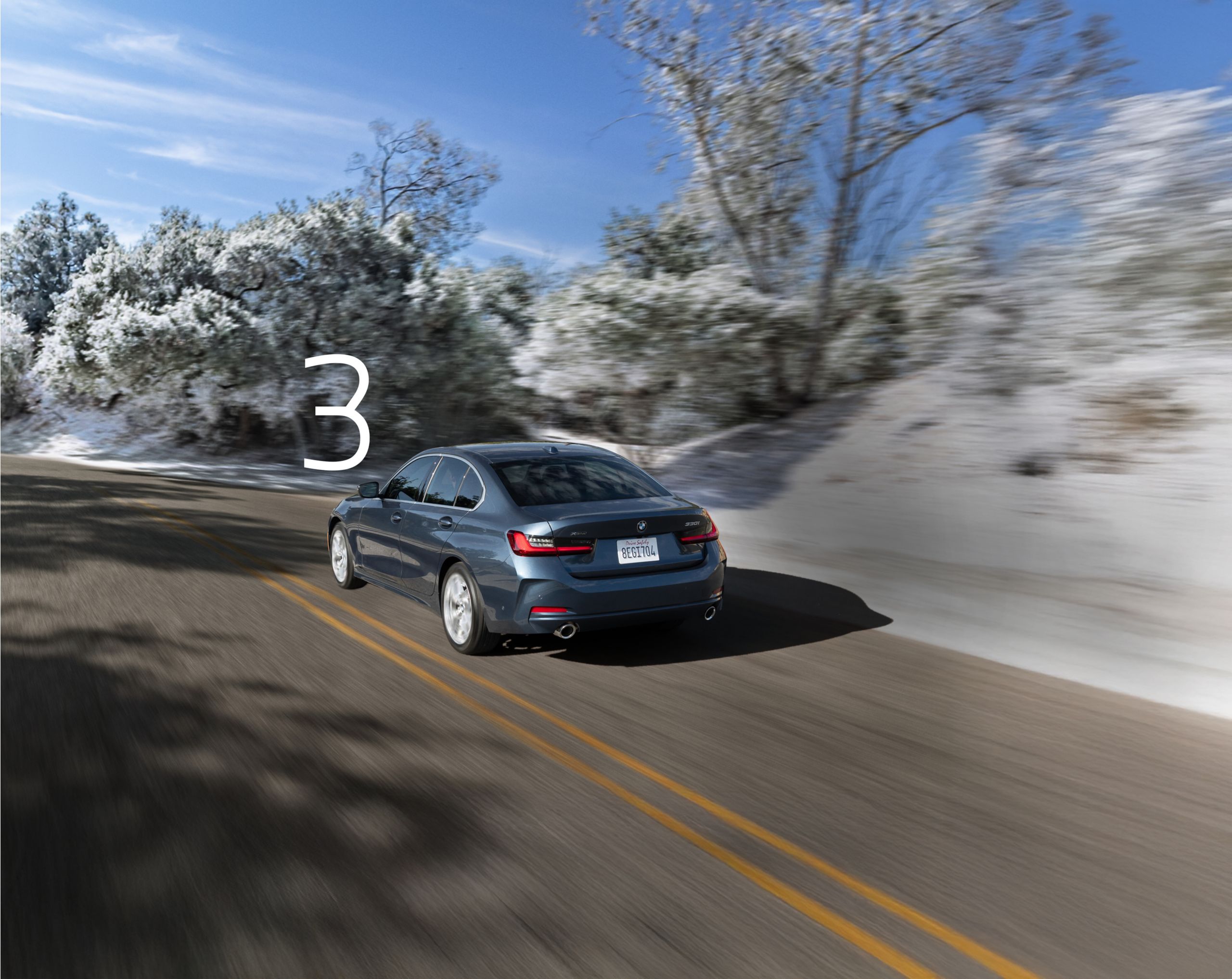 Rear view of a 2026 BMW 330i xDrive driving on a snowy, tree-lined street