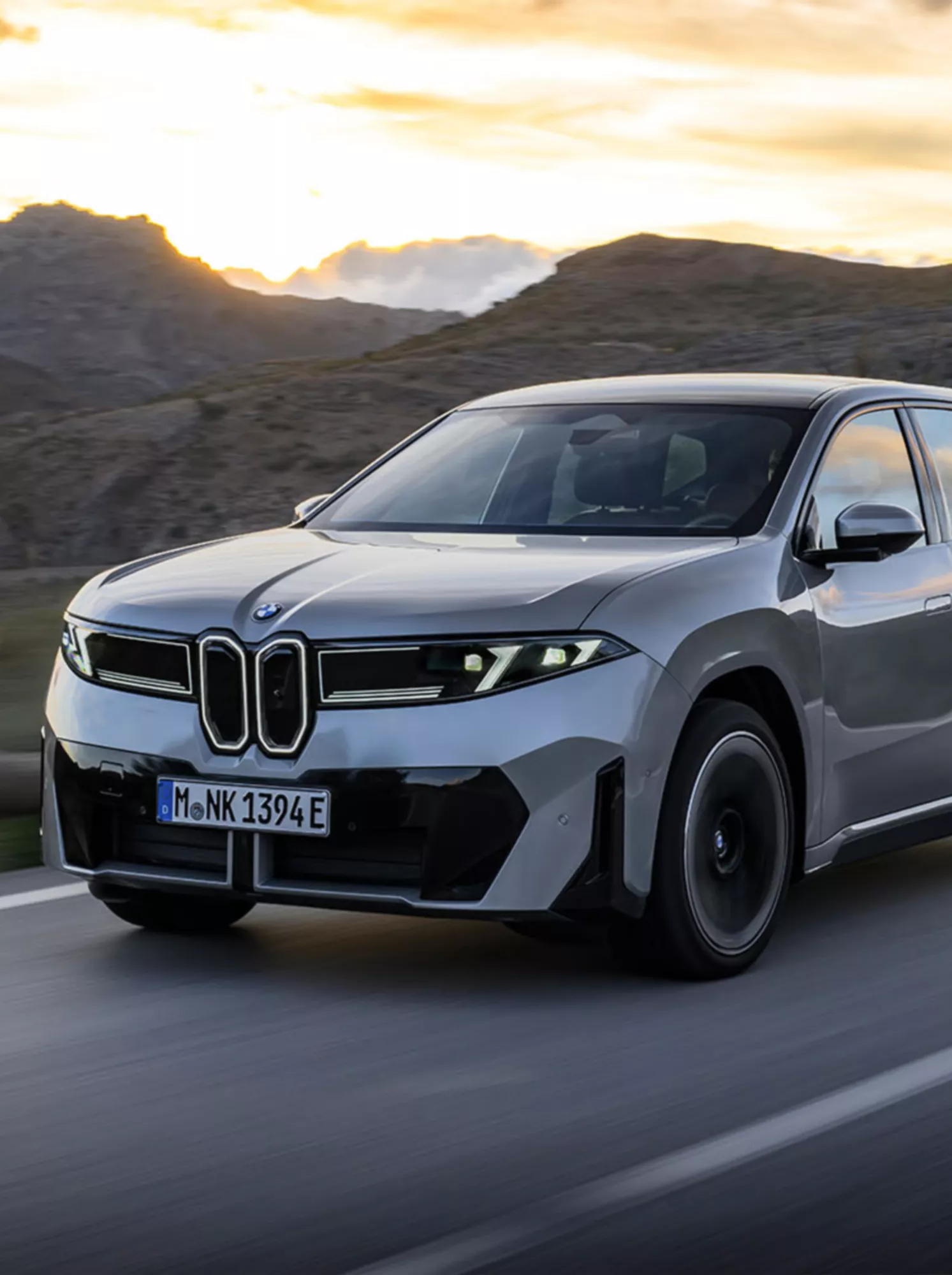 En grå BMW iX3 sett skrått forfra i solnedgang 