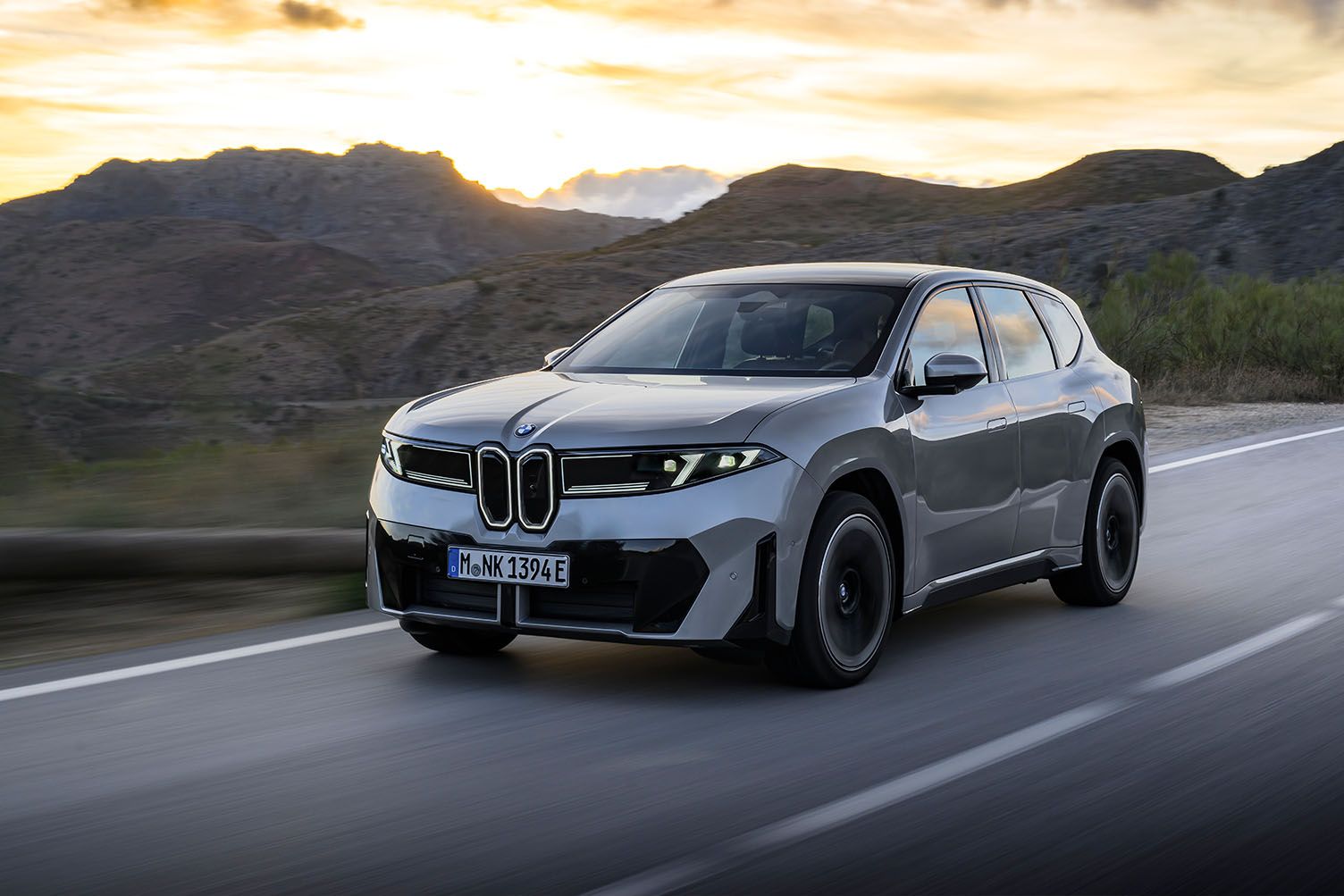 En grå BMW iX3 sett skrått forfra i solnedgang 