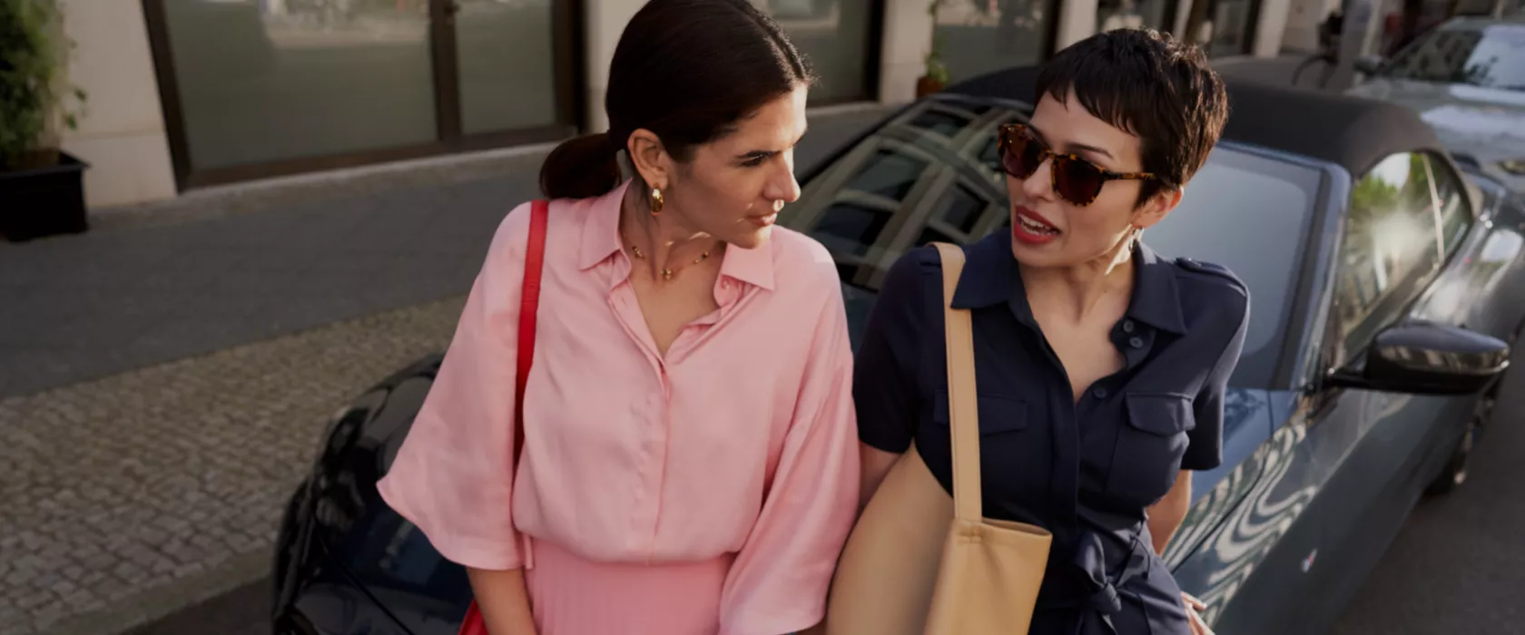 Two women leaning against a BMW convertible