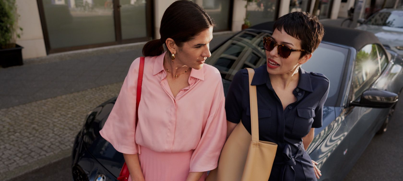 Two women leaning against a BMW convertible