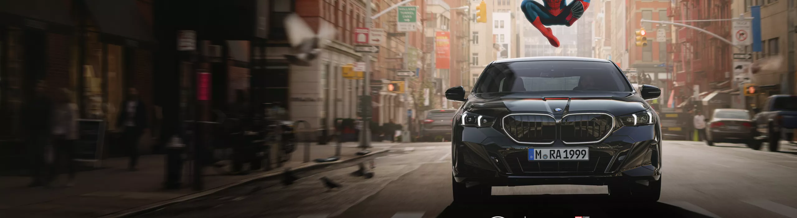 Eine schwarze BMW i5 Limousine fährt auf einer Stadtstraße zwischen hohen Gebäuden. Über dem Fahrzeug springt Spider-Man. Im unteren Bereich befinden sich die BMW- und Spider-Man-Logos.