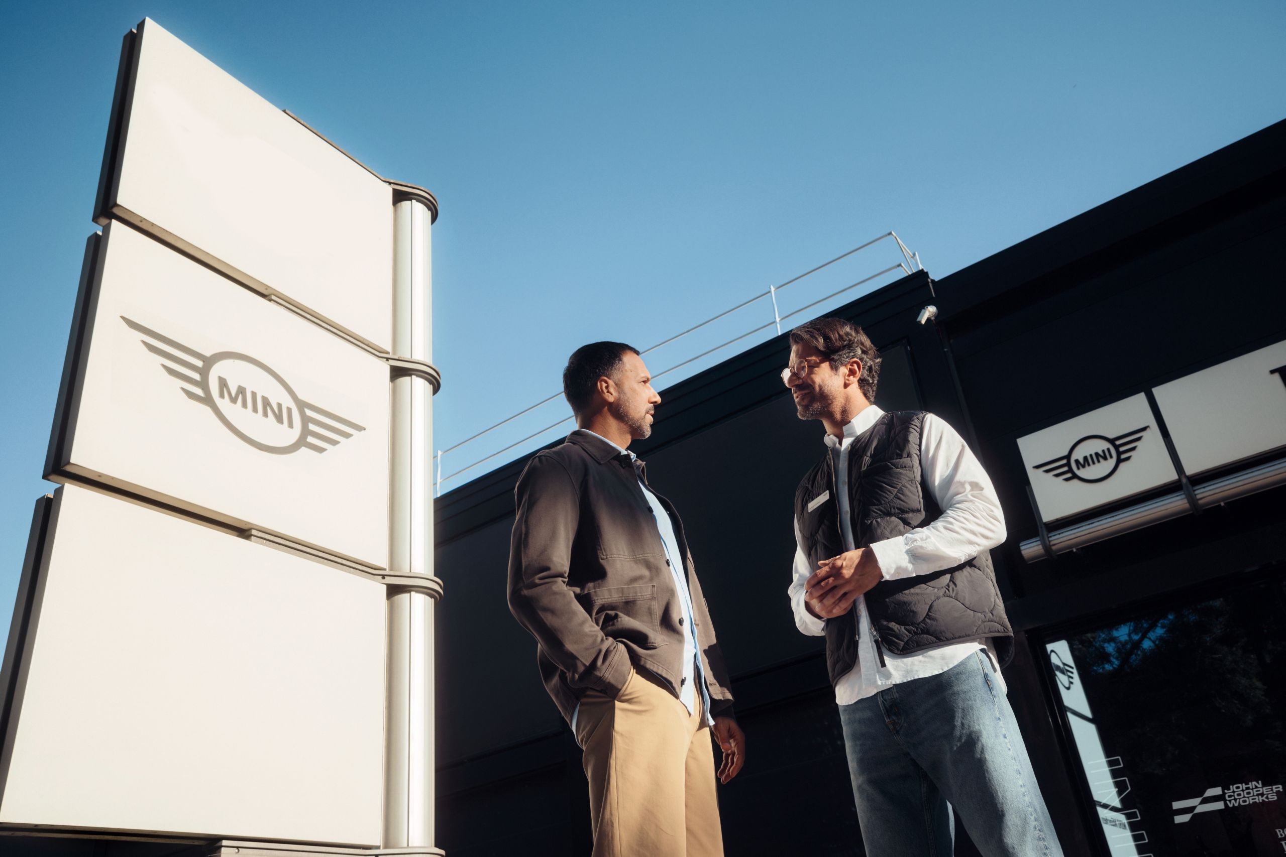 An up angle shot of two men talking outside a MINI dealership