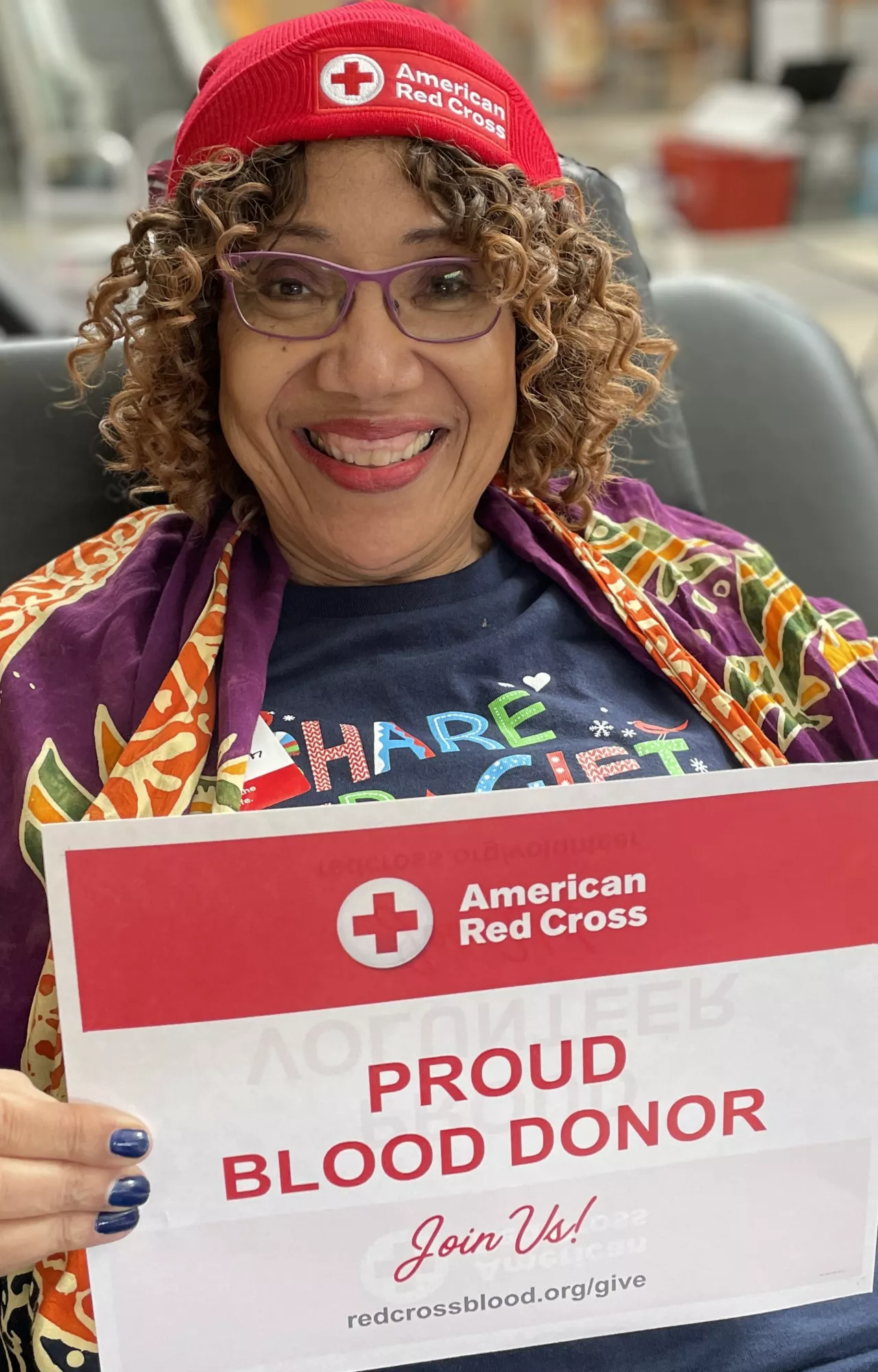 A woman smiling and holding up her blood donor certificate