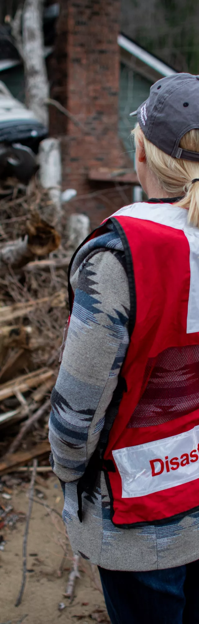 A shot from behind of a Red Cross worker looking at the damage after a natural disaster