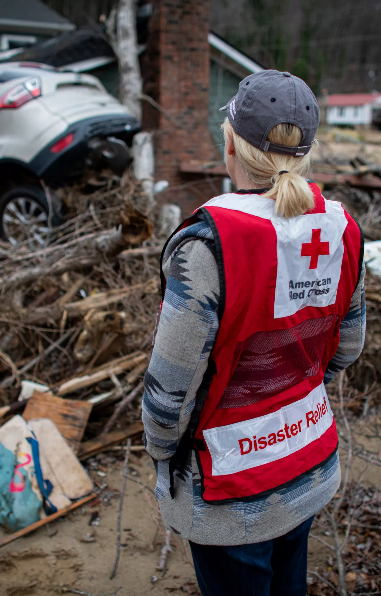 A shot from behind of a Red Cross worker looking at the damage after a natural disaster
