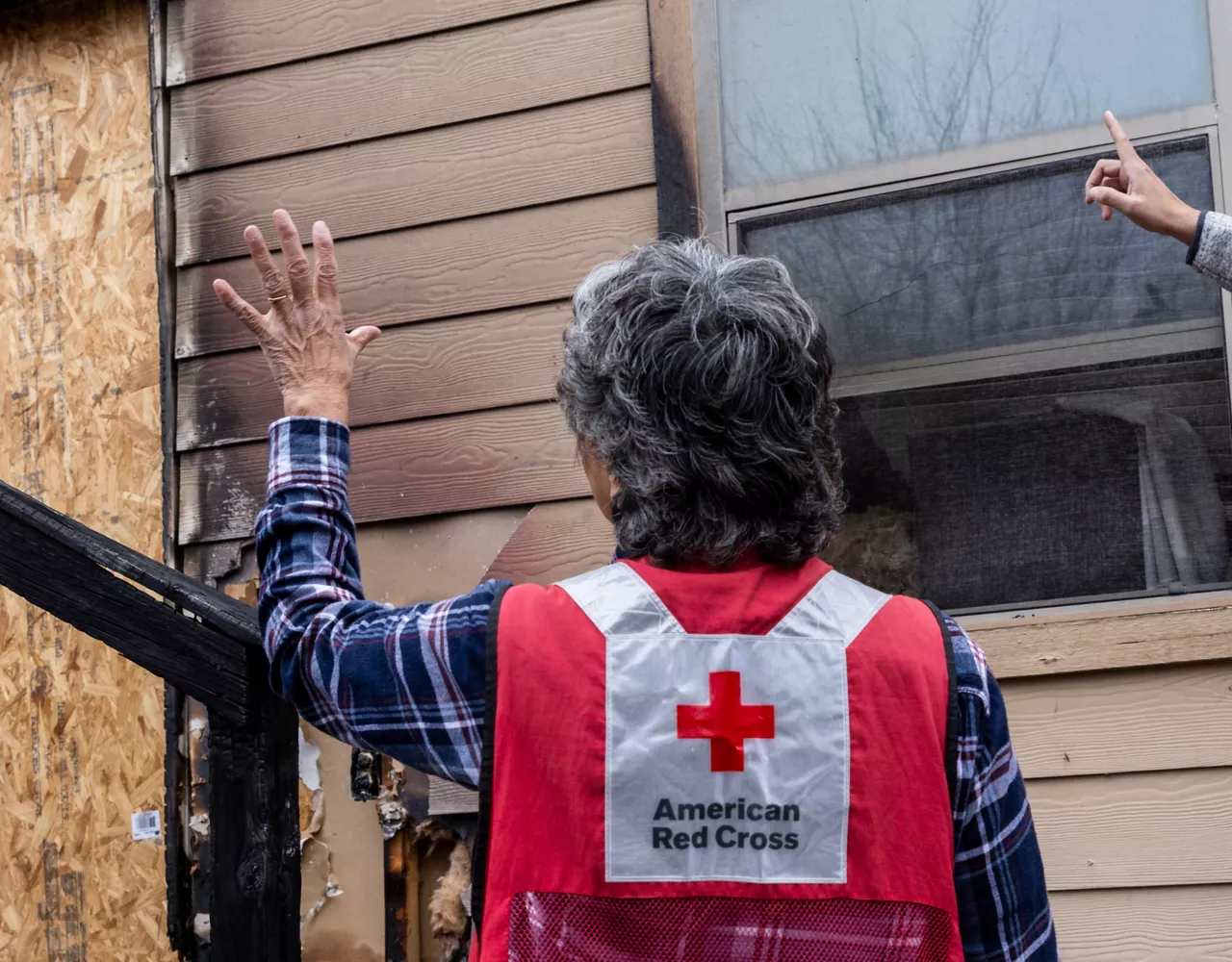 Two Red Cross workers gesturing and looking at a house with fire damage