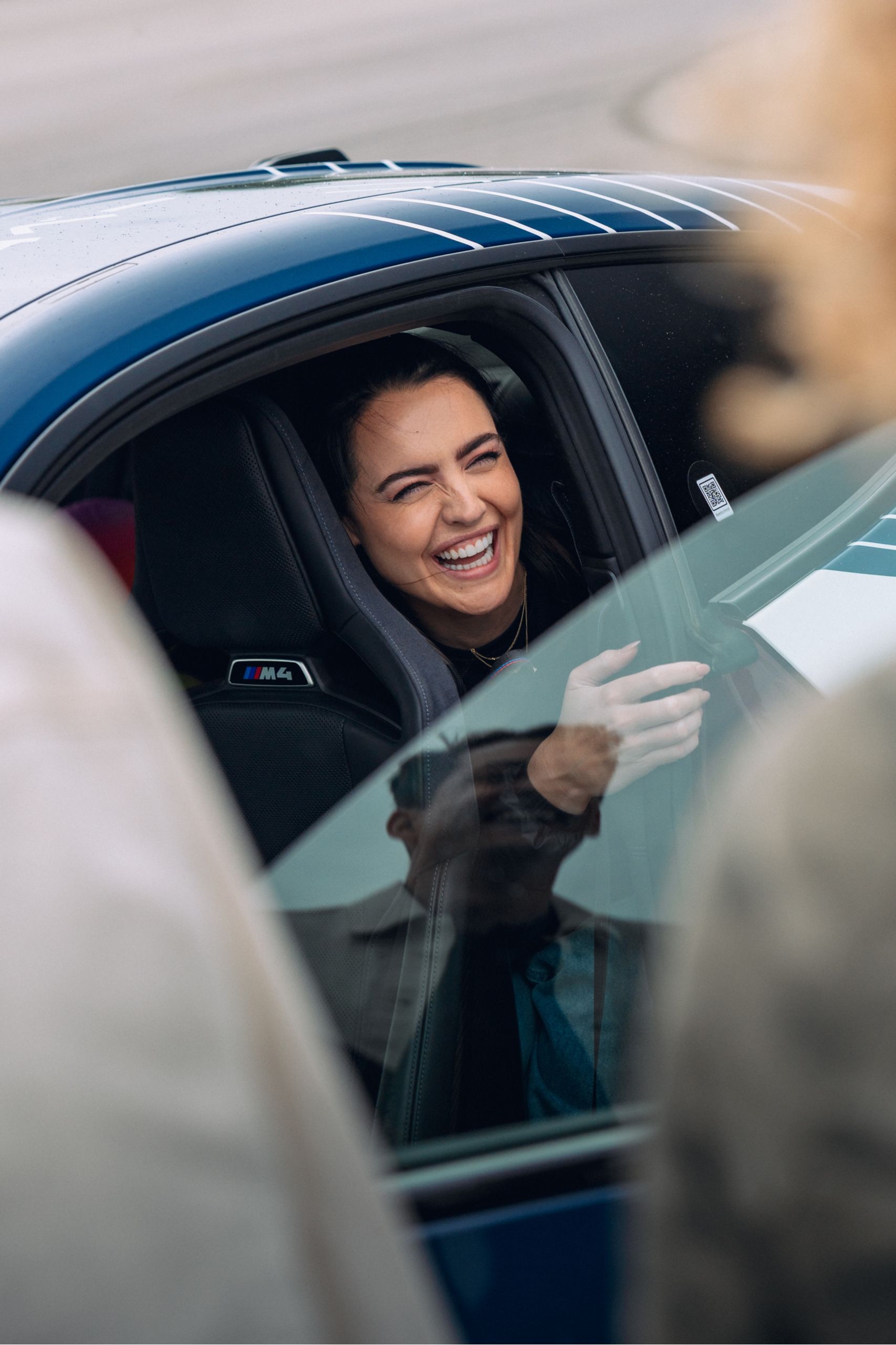 A woman laughing as she climbs out of the backseat of a BMW M4