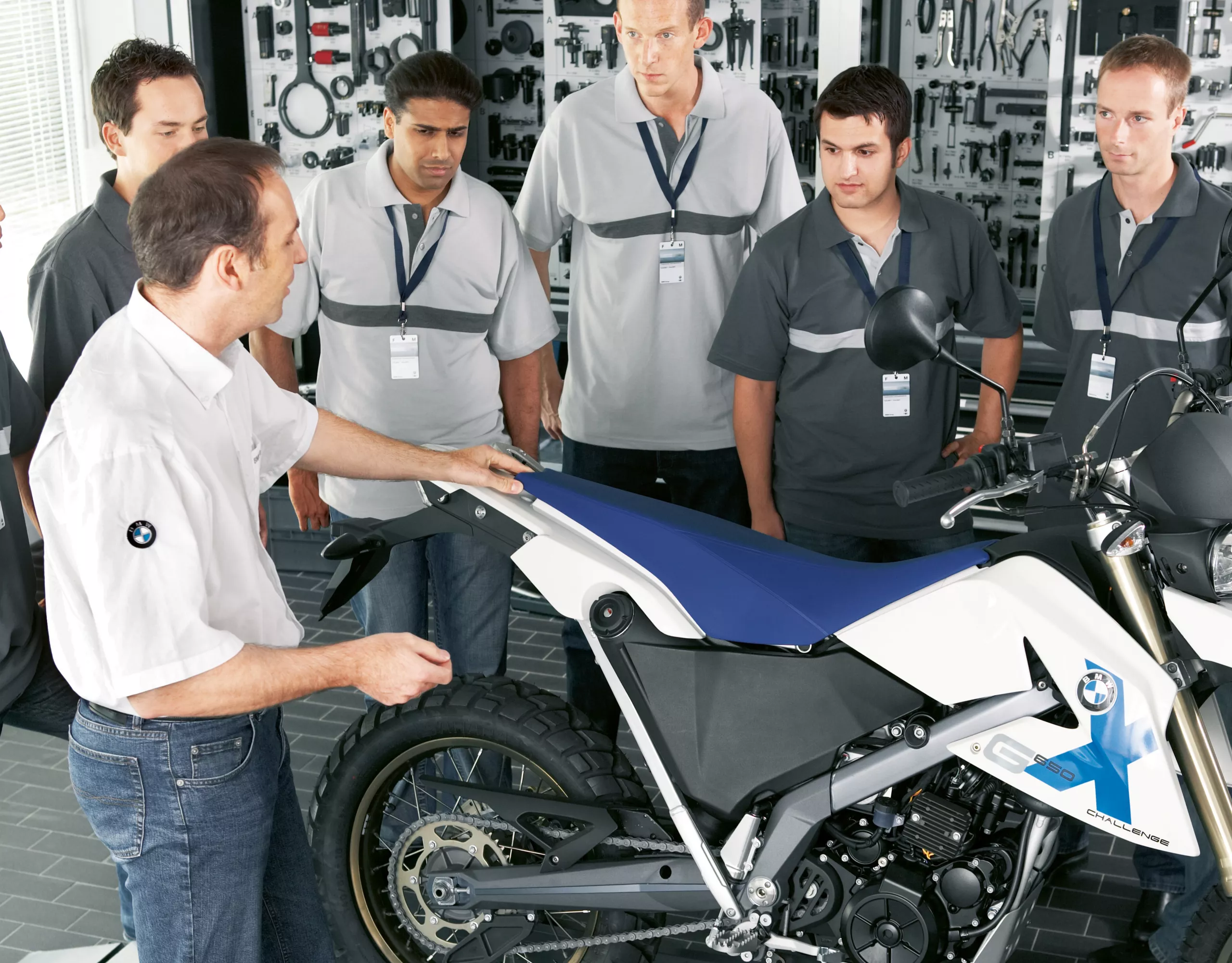 A BMW technician gestures towards a BMW motorcycle as he  speaks to a group of trainees