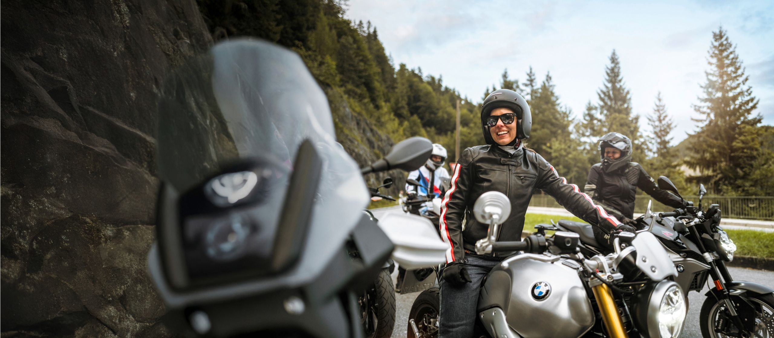 A group of BMW motorcycle drivers smiling and parked on the side of the road