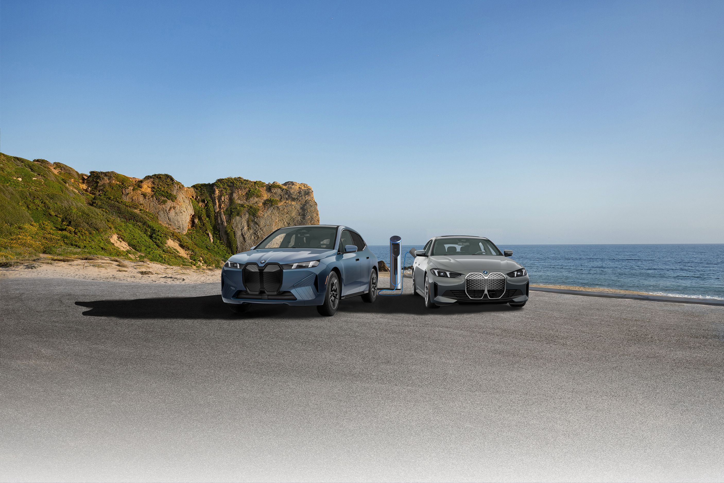 A BMW iX and BMW i4 parked and charging in a parking area next to a large body of water