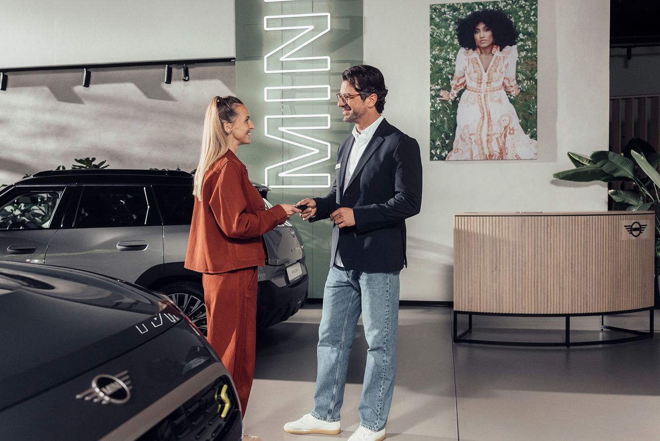 A woman receives keys from a representative at a MINI dealership