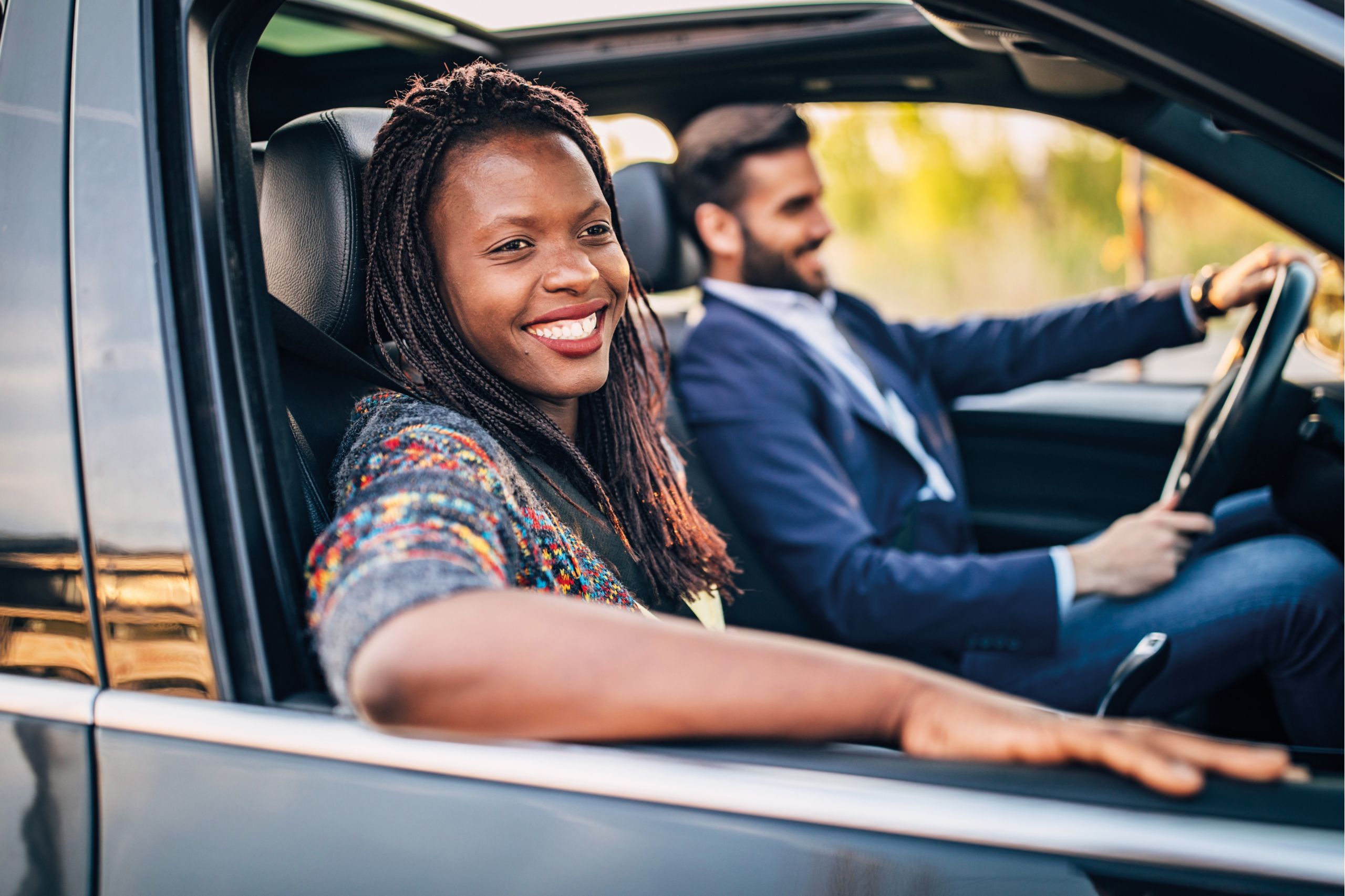 A woman in the passenger seat looks out the window and smiles as a man is driving in the background