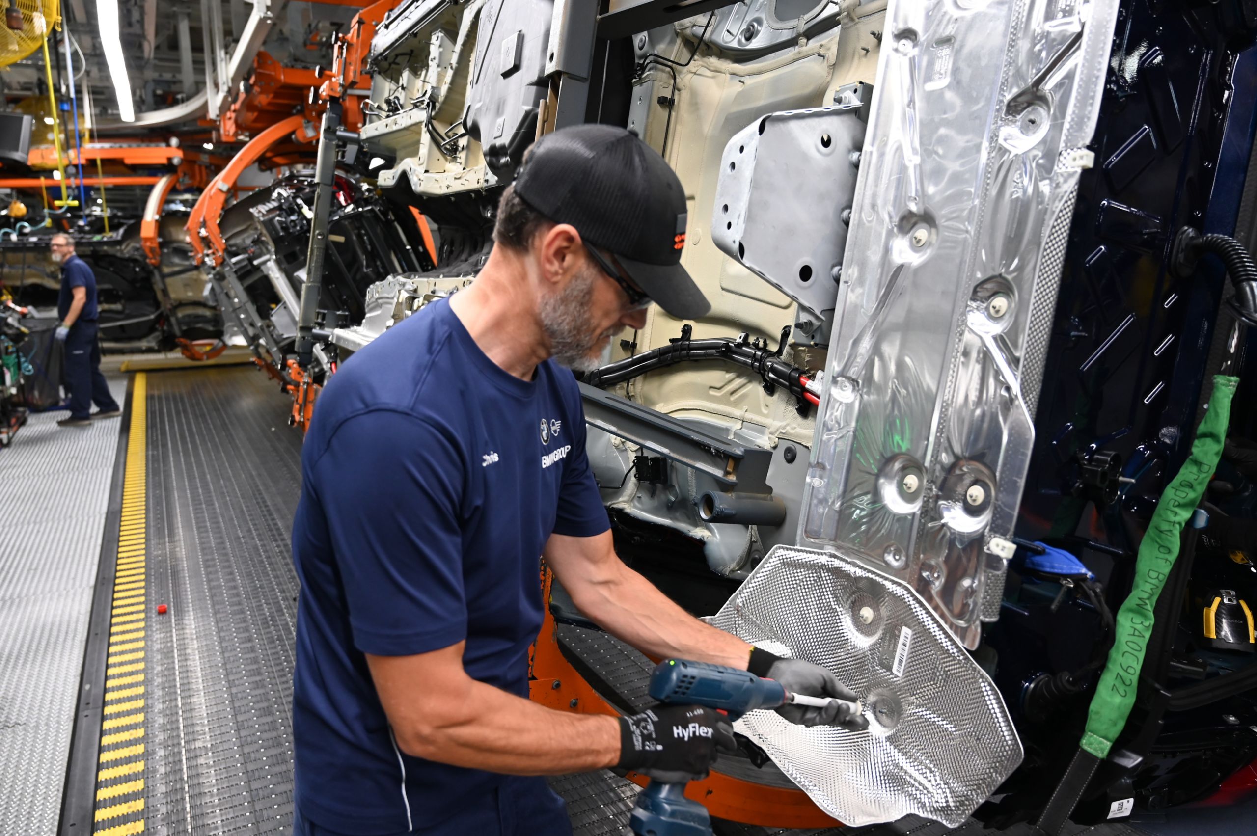 A young man in a BMW assembly plant screw a part into the body of a vehicle