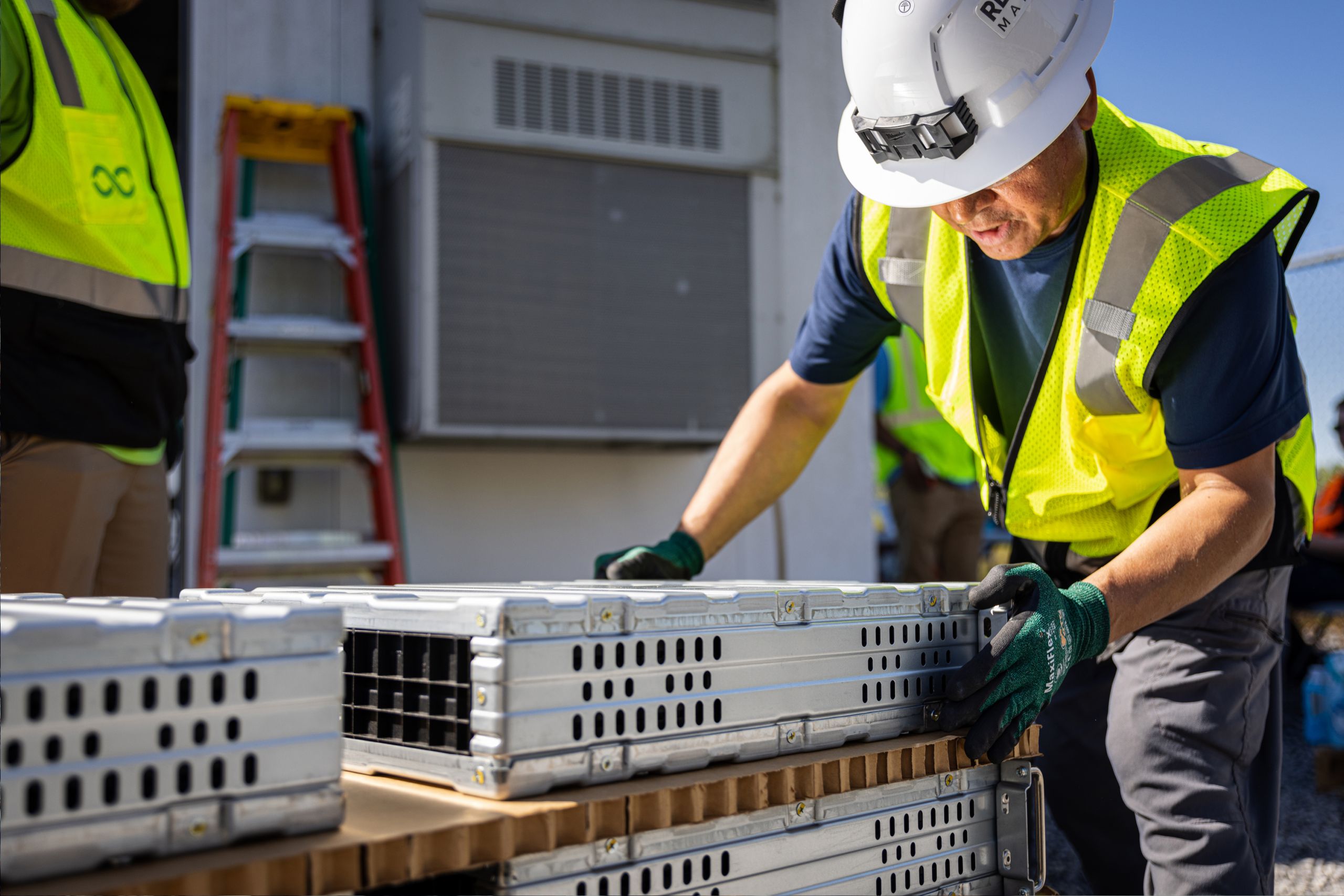 A person wearing a safety vest and gloves placing their hands on a large lithium ion battery cell