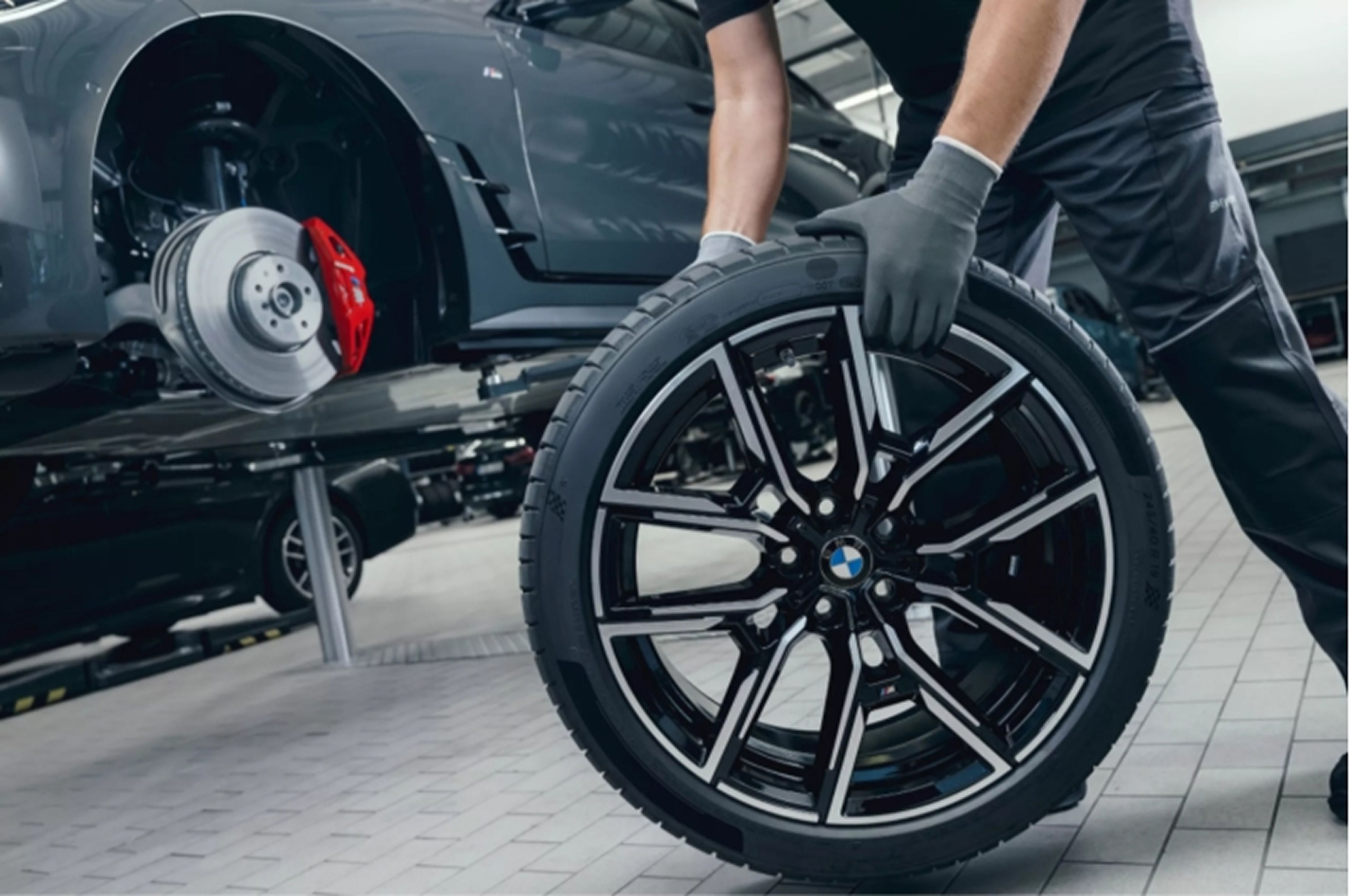 Someone wearing gloves rolls a BMW tire across a factory floor