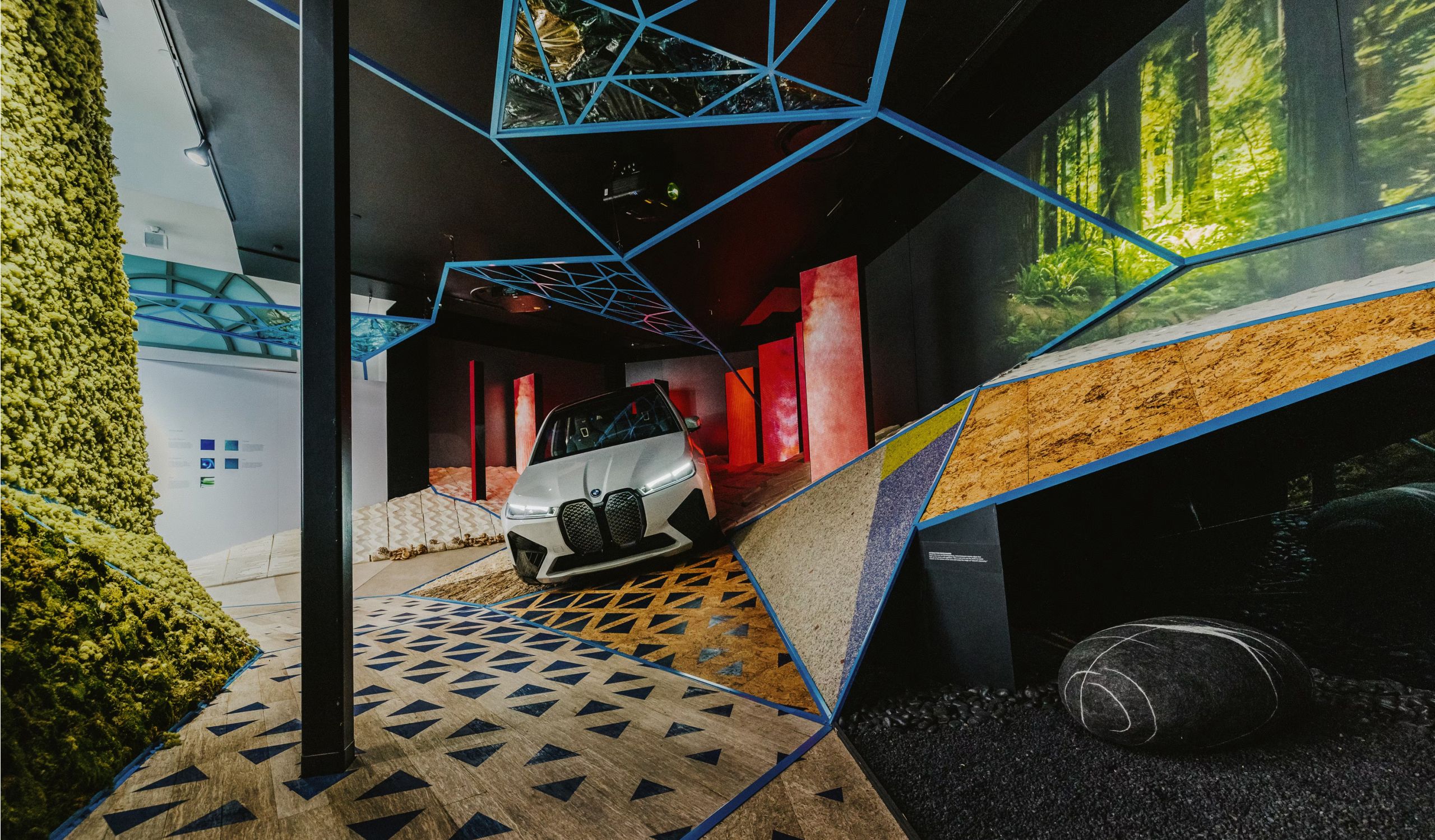 A BMW iX parked within a MATERIA installation, featuring abstract shapes and angles made from different materials.