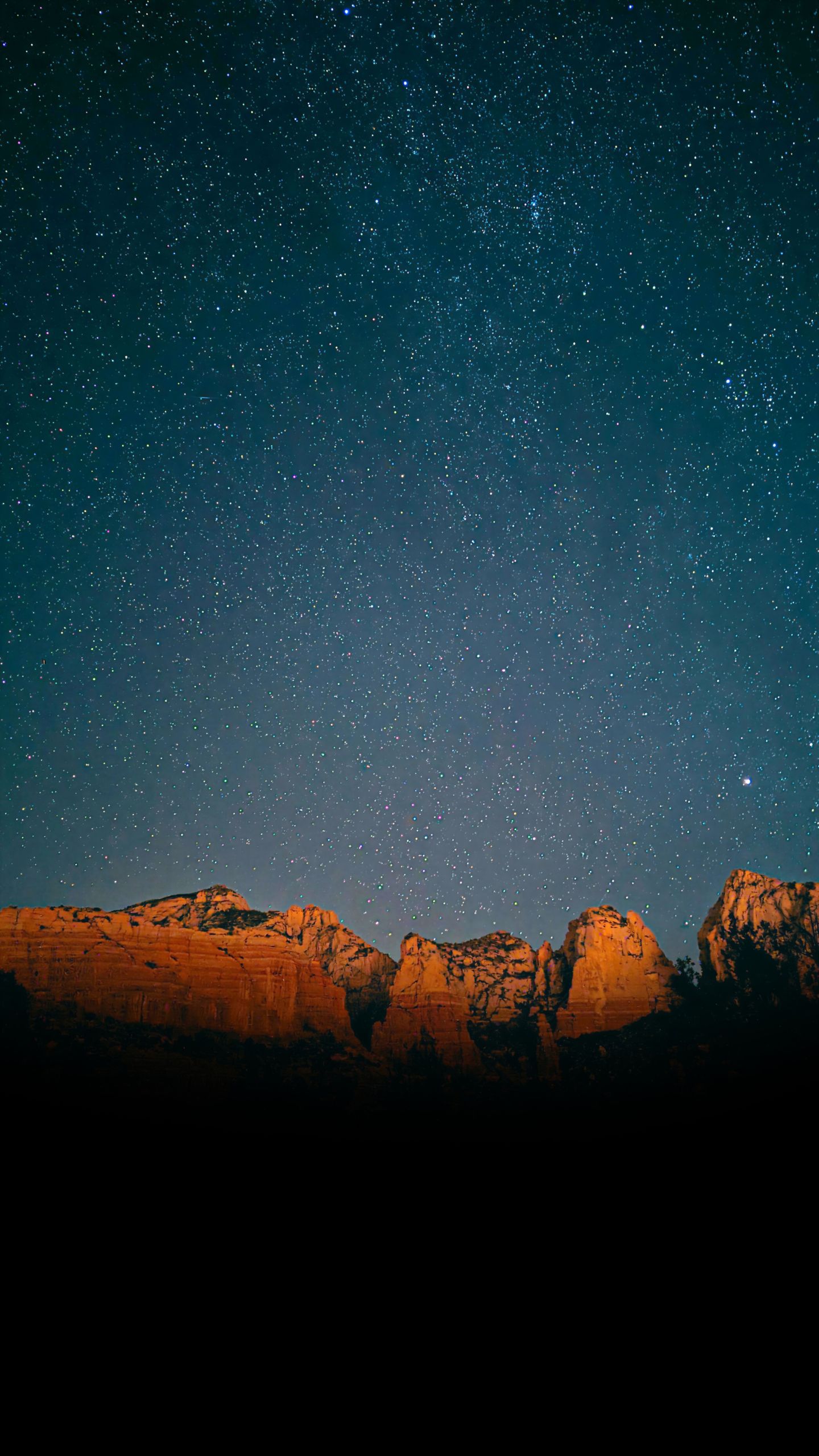 A beautifully lit scene of a large mountain canyon wall at night with a starry sky behind it