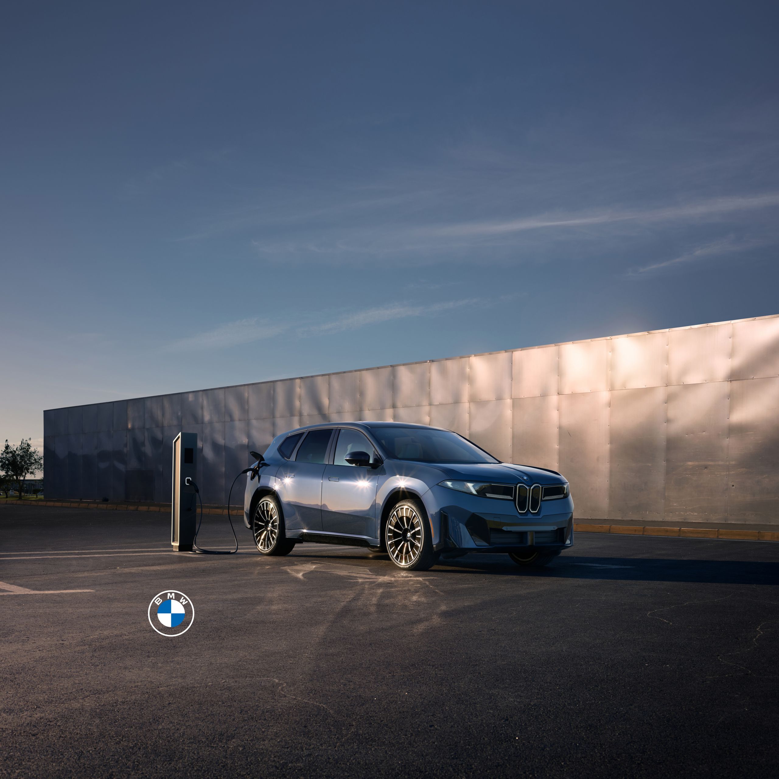A BMW iX plugged into a charging station in front of a large metal wall